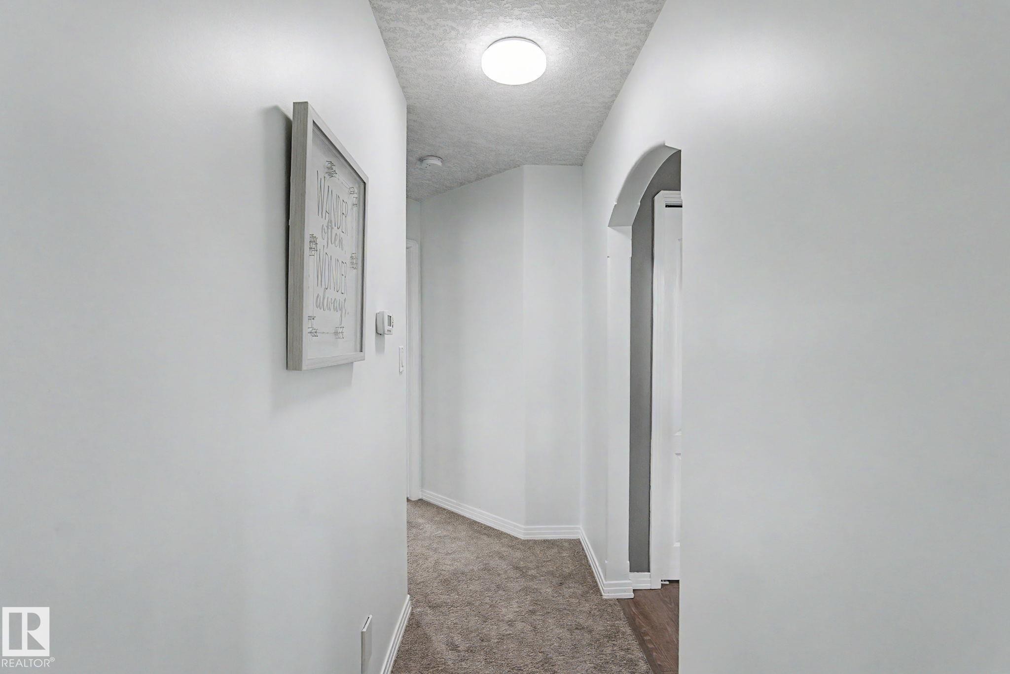 Hallway featuring light gray walls, textured ceiling, a circular flush-mount light fixture, and plush carpet flooring - 1619 Welbourn Cove, Edmonton, AB