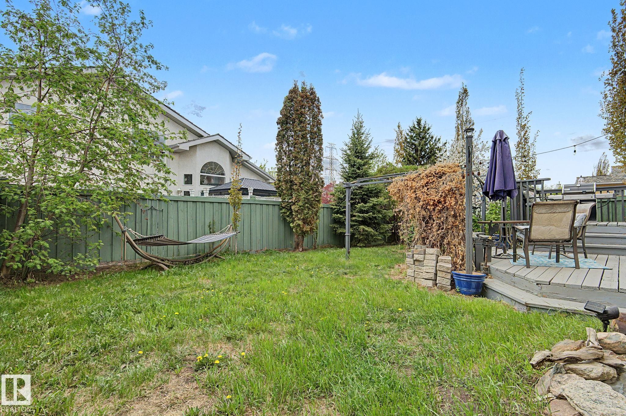 Expansive green space featuring a multi-level wood deck, privacy fencing, mature trees, and a stone-edged garden area - 1619 Welbourn Cove, Edmonton, AB