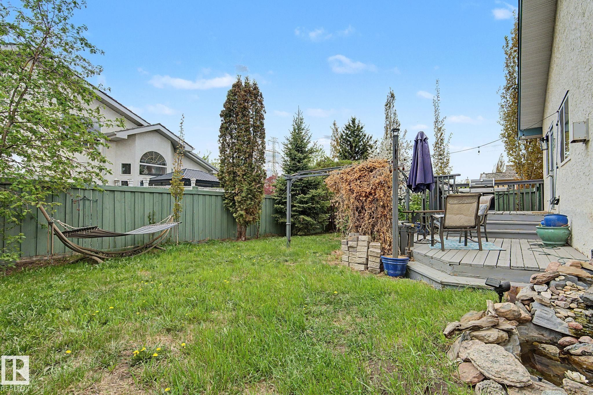 Spacious backyard featuring a multi-level wood deck, a stone water feature, a green privacy fence, and mature landscaping - 1619 Welbourn Cove, Edmonton, AB
