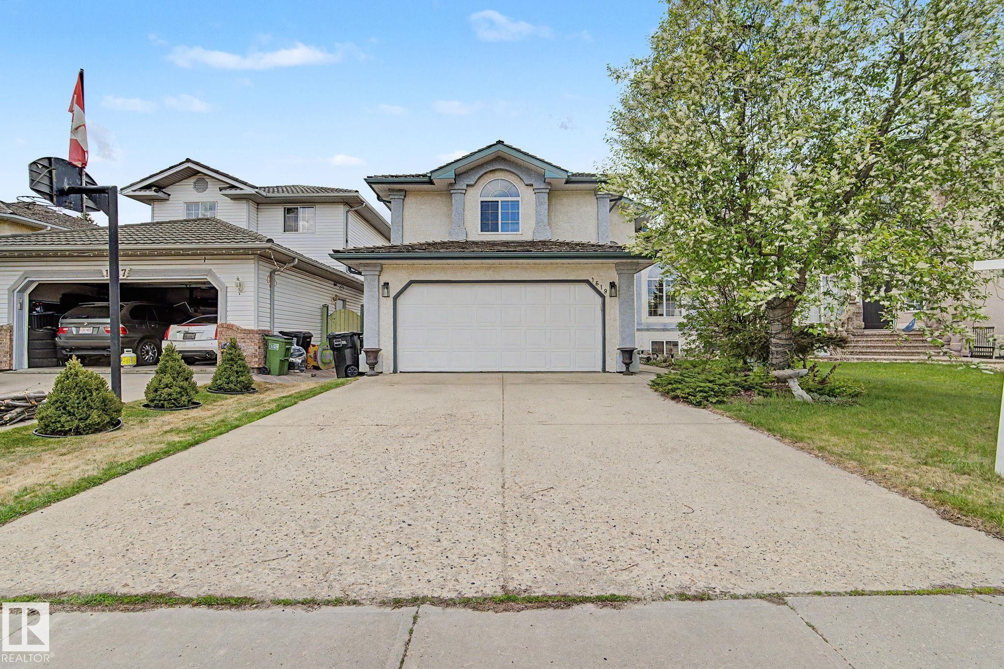 Two-story stucco exterior with a prominent arched window feature, a two-car garage, and a concrete driveway - 1619 Welbourn Cove, Edmonton, AB