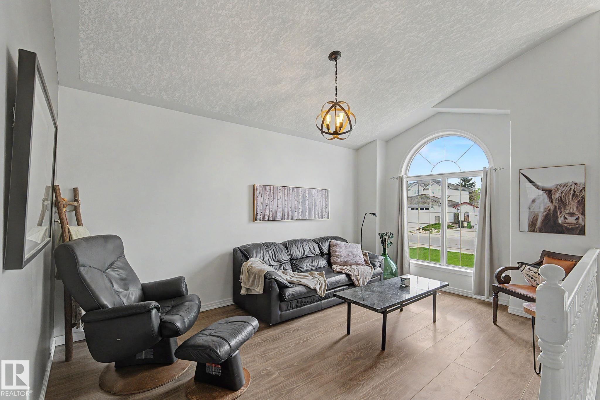 Vaulted ceiling living area featuring a large arched window, wood-finish flooring, and a decorative pendant light fixture - 1619 Welbourn Cove, Edmonton, AB