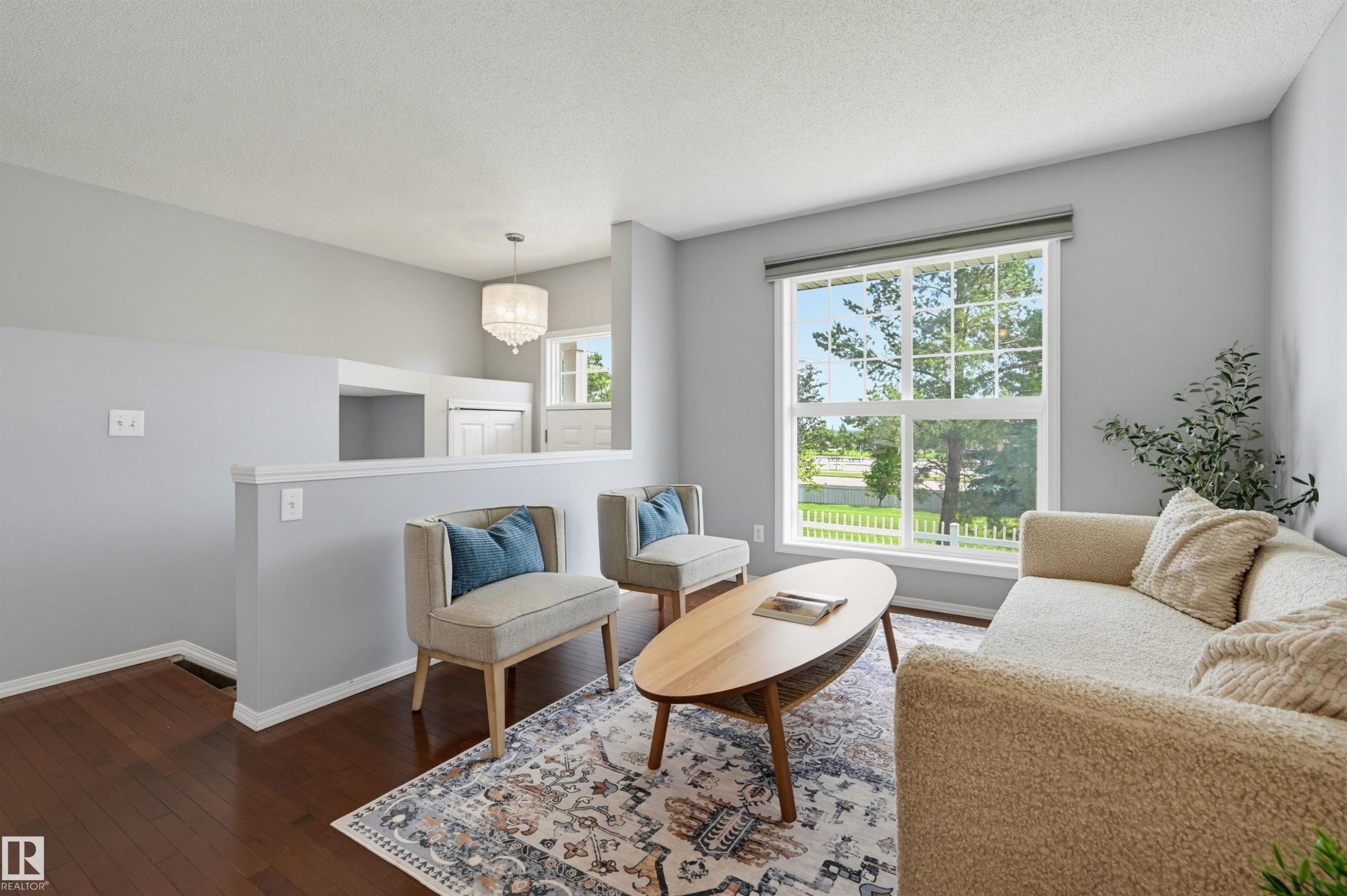 Spacious living area featuring rich wood-finish flooring, a large window, a partial wall, and a built-in light fixture - 126 2051 Towne Centre Boulevard, Edmonton, AB