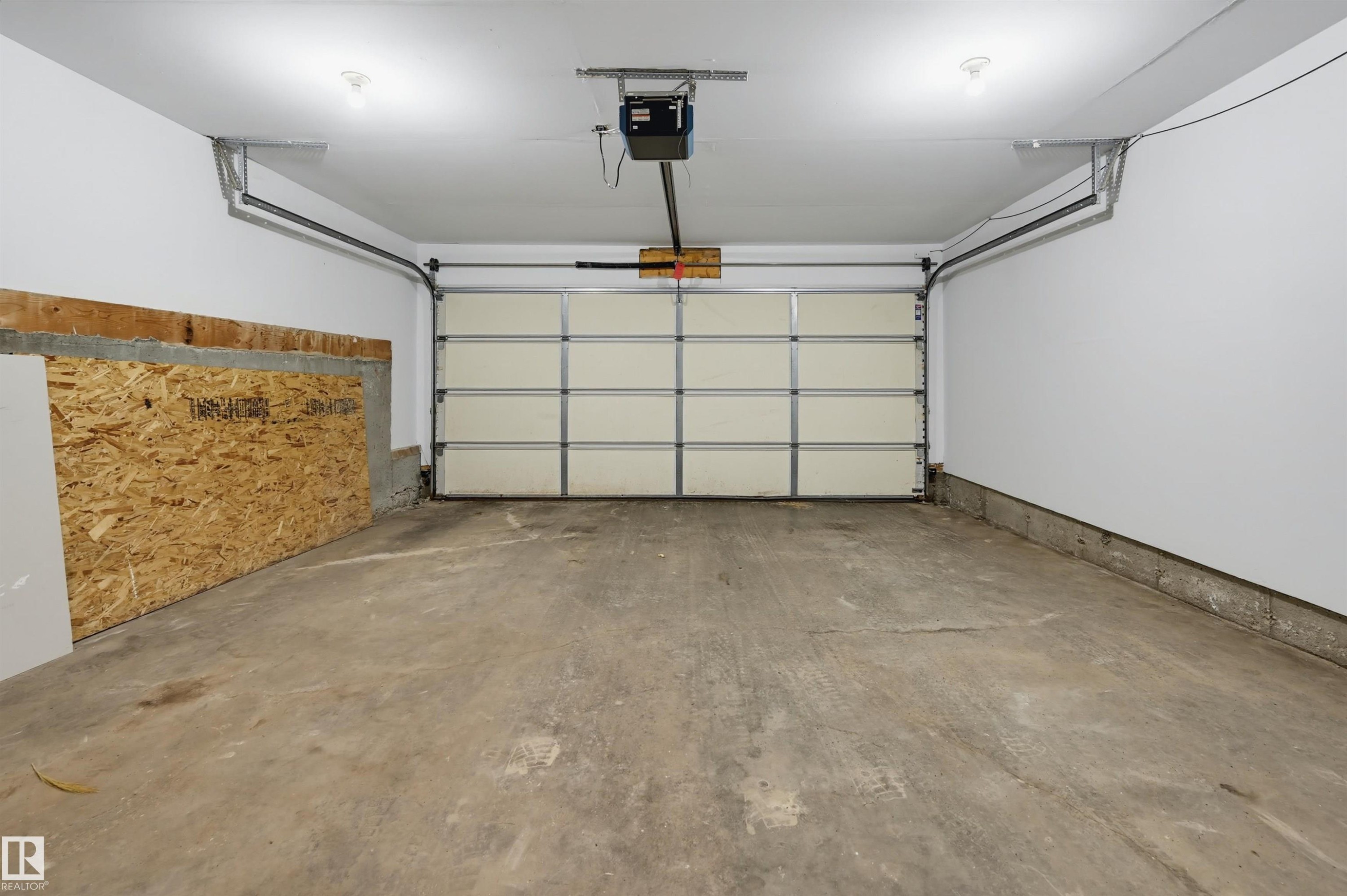 Spacious garage featuring a concrete floor, white painted walls, and an automatic garage door opener - 126 2051 Towne Centre Boulevard, Edmonton, AB