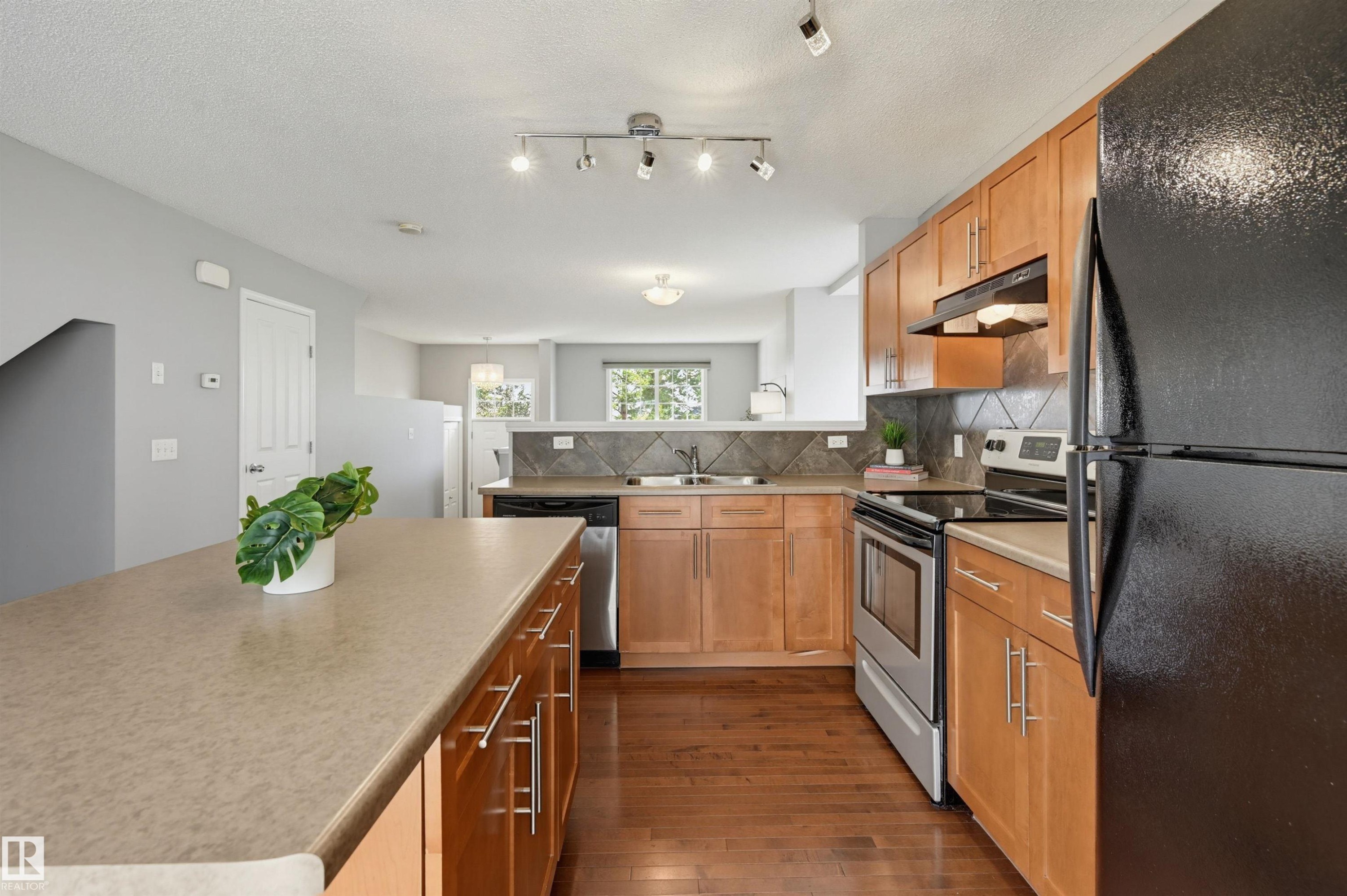 Kitchen featuring light wood cabinetry, dark wood-finish flooring, a black refrigerator, and stainless steel appliances - 126 2051 Towne Centre Boulevard, Edmonton, AB