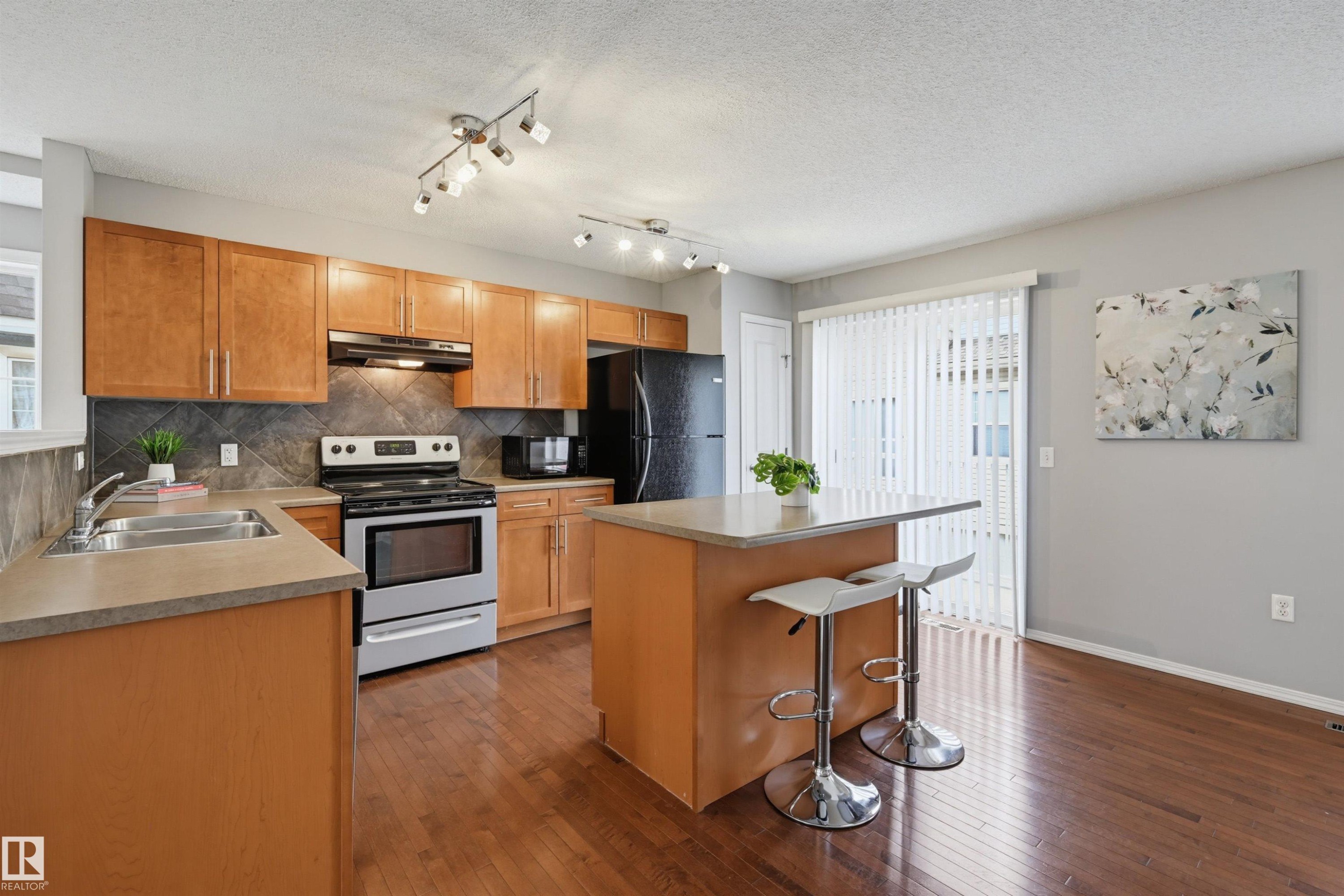 Kitchen featuring wood-finish cabinetry, stainless steel appliances, a dark tile backsplash, and a light-toned countertop - 126 2051 Towne Centre Boulevard, Edmonton, AB