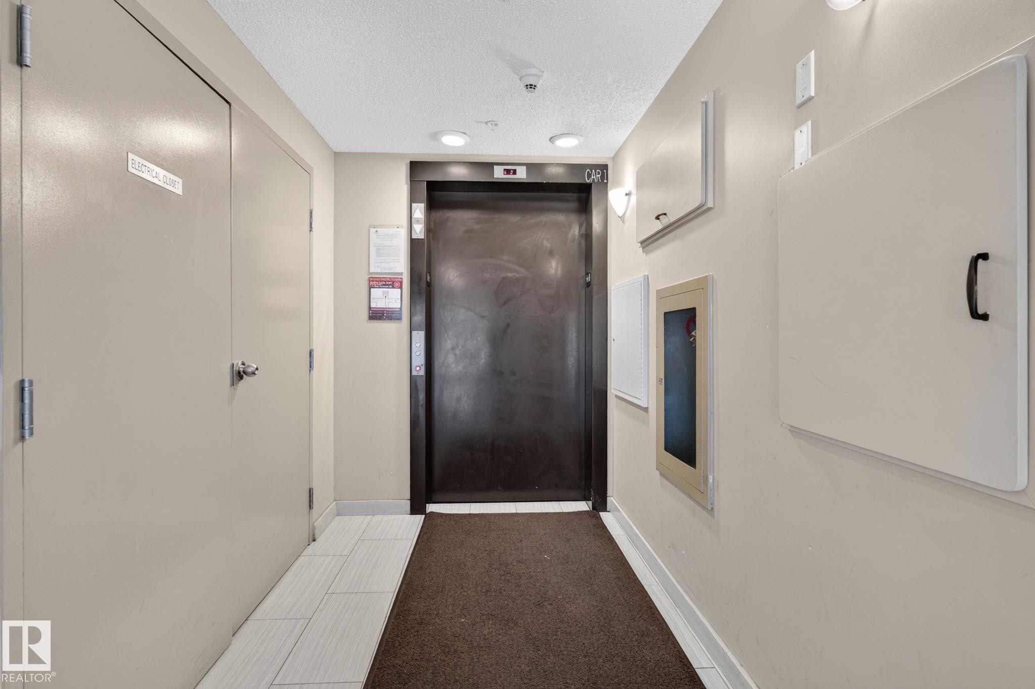 Hallway featuring a dark elevator door, recessed ceiling lighting, and light-toned wall panels - 415 111 Watt Common, Edmonton, AB