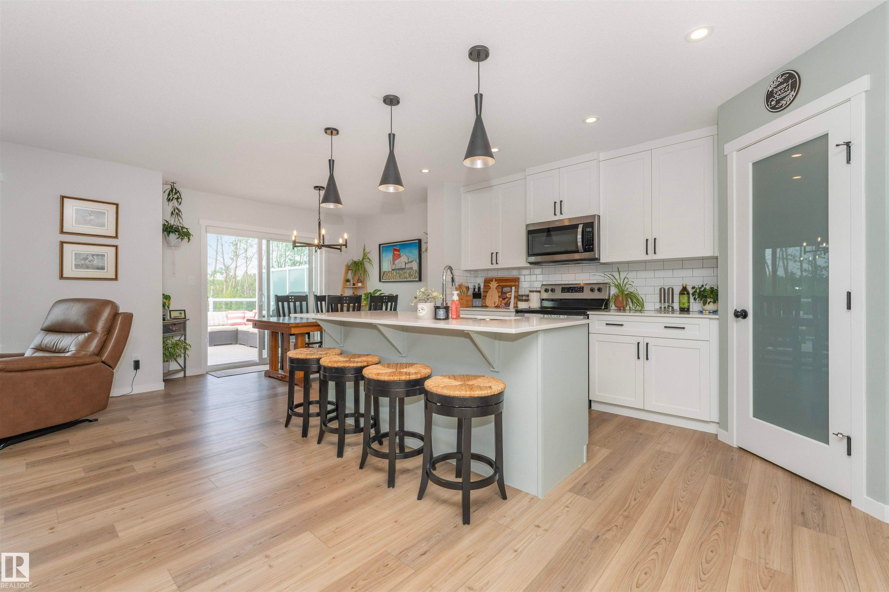 Open-concept kitchen featuring an expansive island with pendant lighting, white shaker cabinetry, stainless steel appliances, and wood-finish flooring - 102 Horton Way, Ardrossan, AB