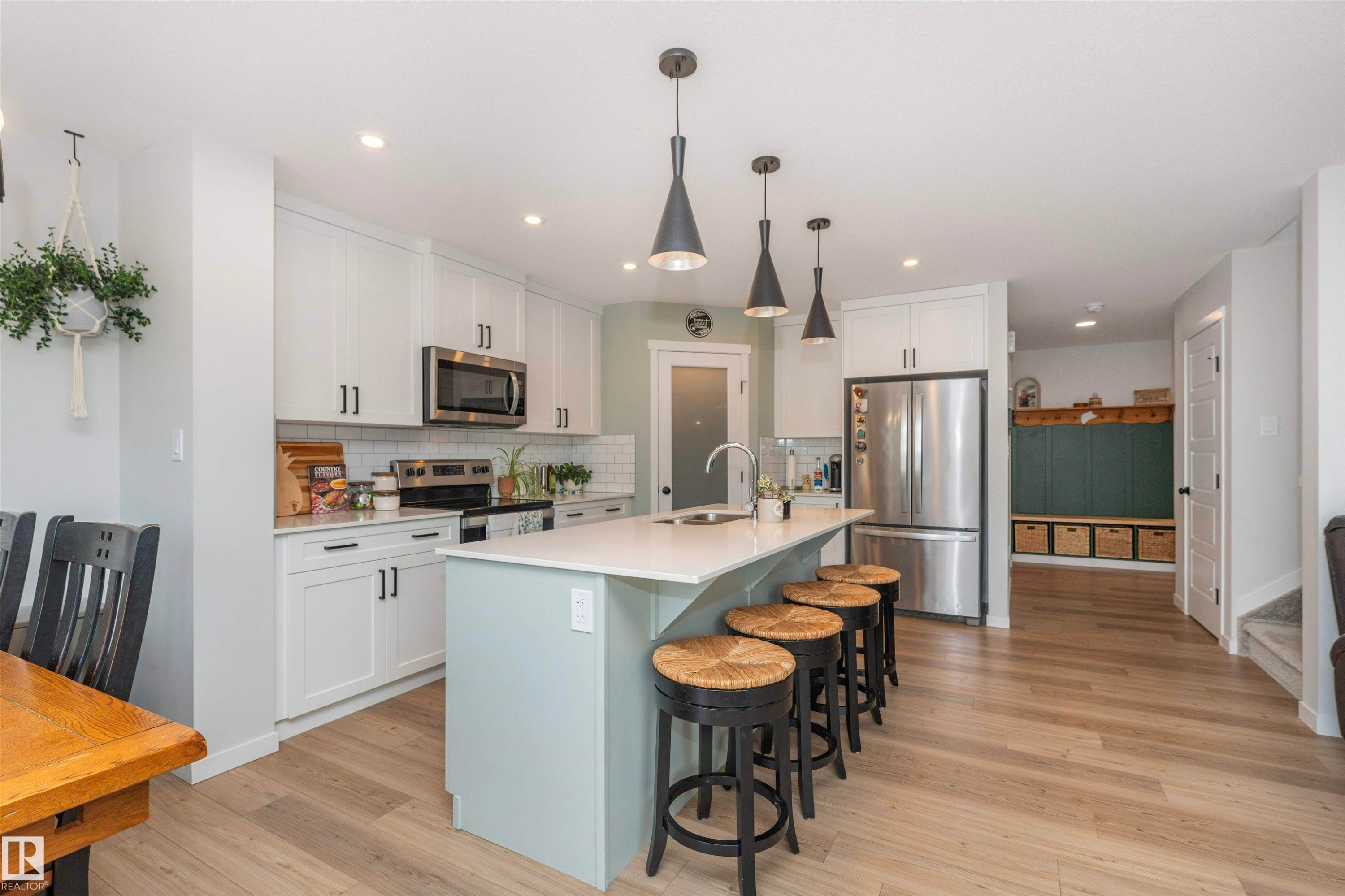Open-concept kitchen featuring an island with seating, white shaker-style cabinetry, stainless steel appliances, and wood-finish flooring - 102 Horton Way, Ardrossan, AB