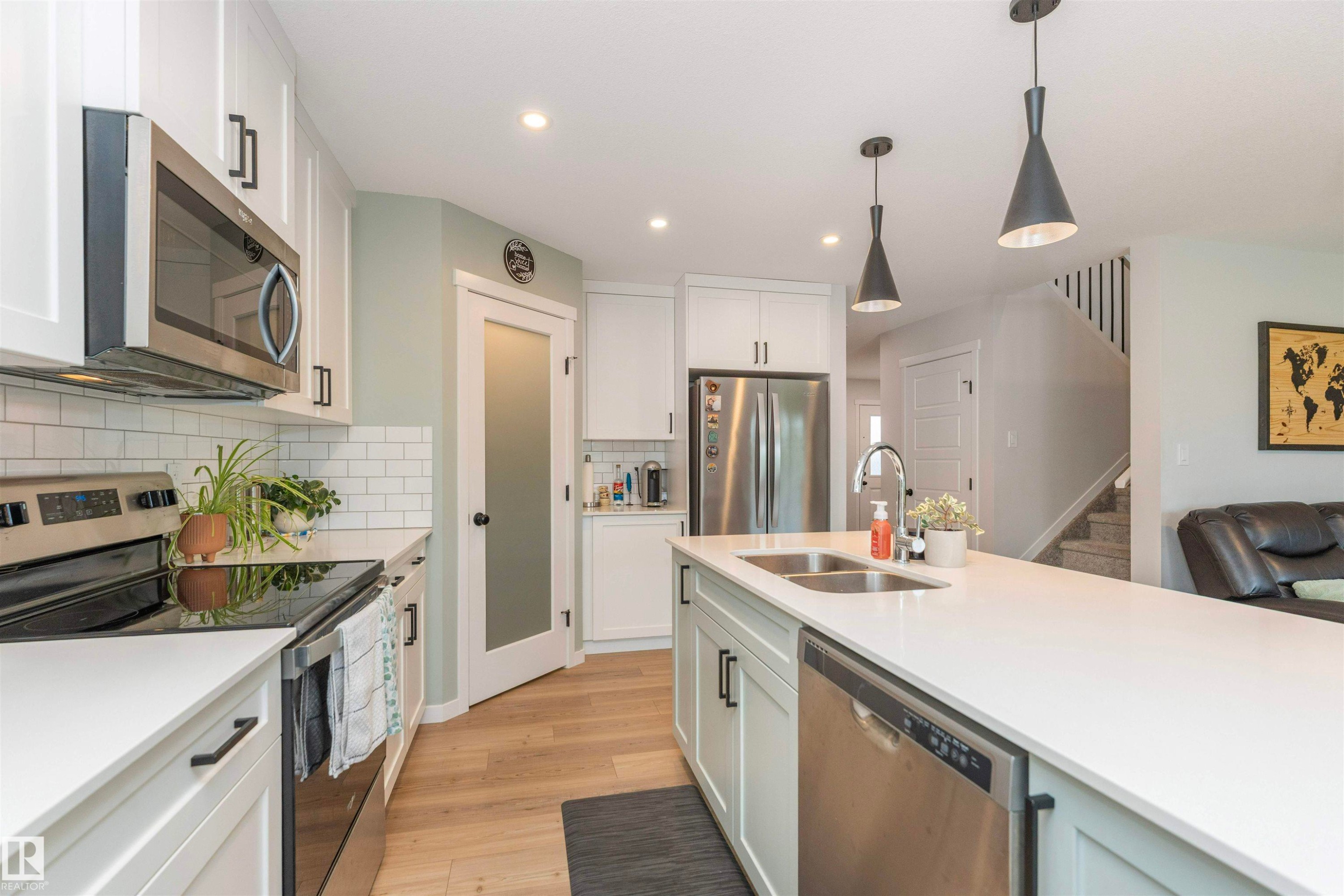 Modern kitchen featuring light wood-finish flooring, white cabinetry with black hardware, stainless steel appliances, and white countertops - 102 Horton Way, Ardrossan, AB