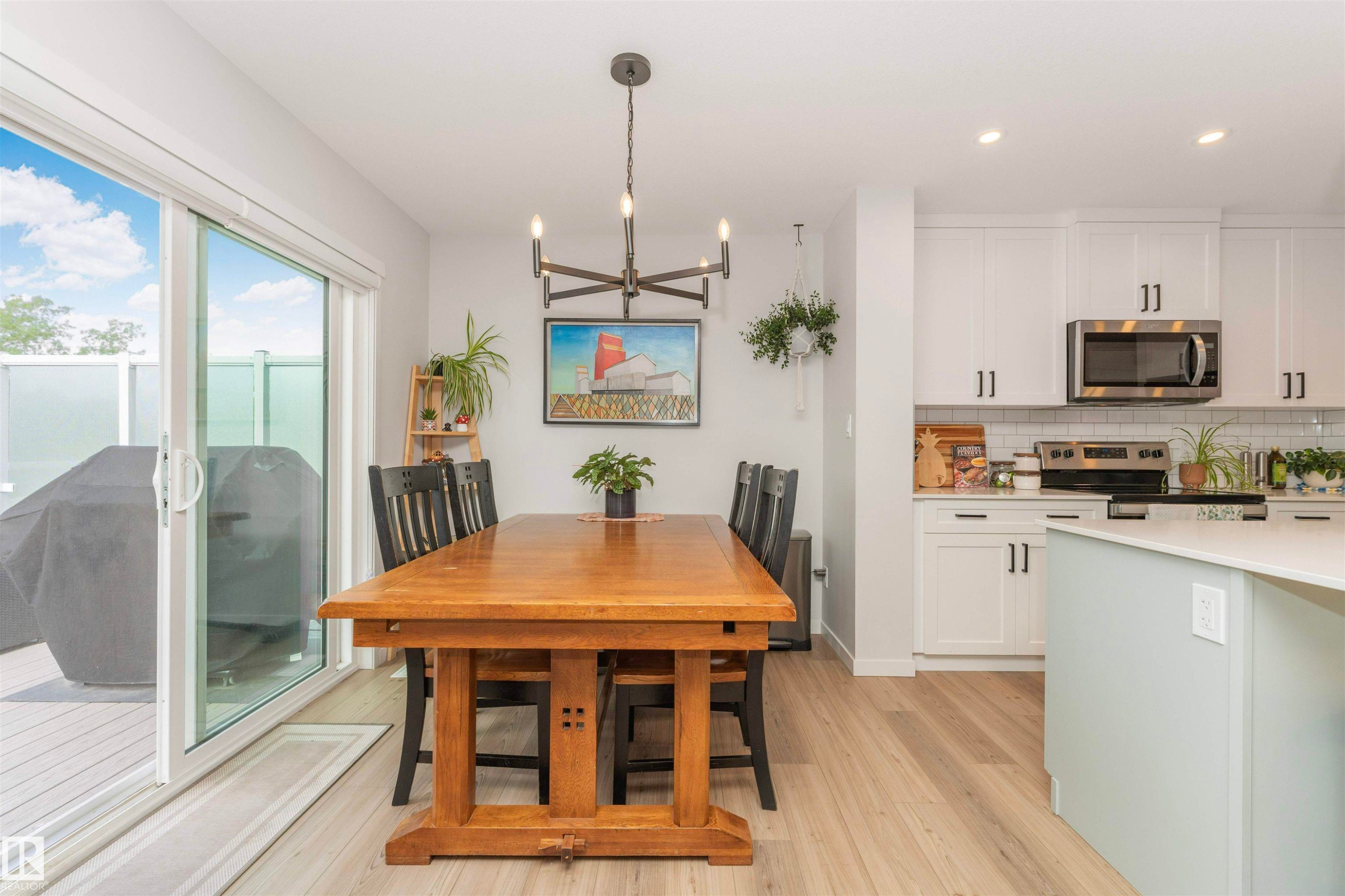 Open concept living area featuring light wood-finish flooring, a contemporary chandelier, recessed lighting, and white cabinetry with stainless steel appliances - 102 Horton Way, Ardrossan, AB
