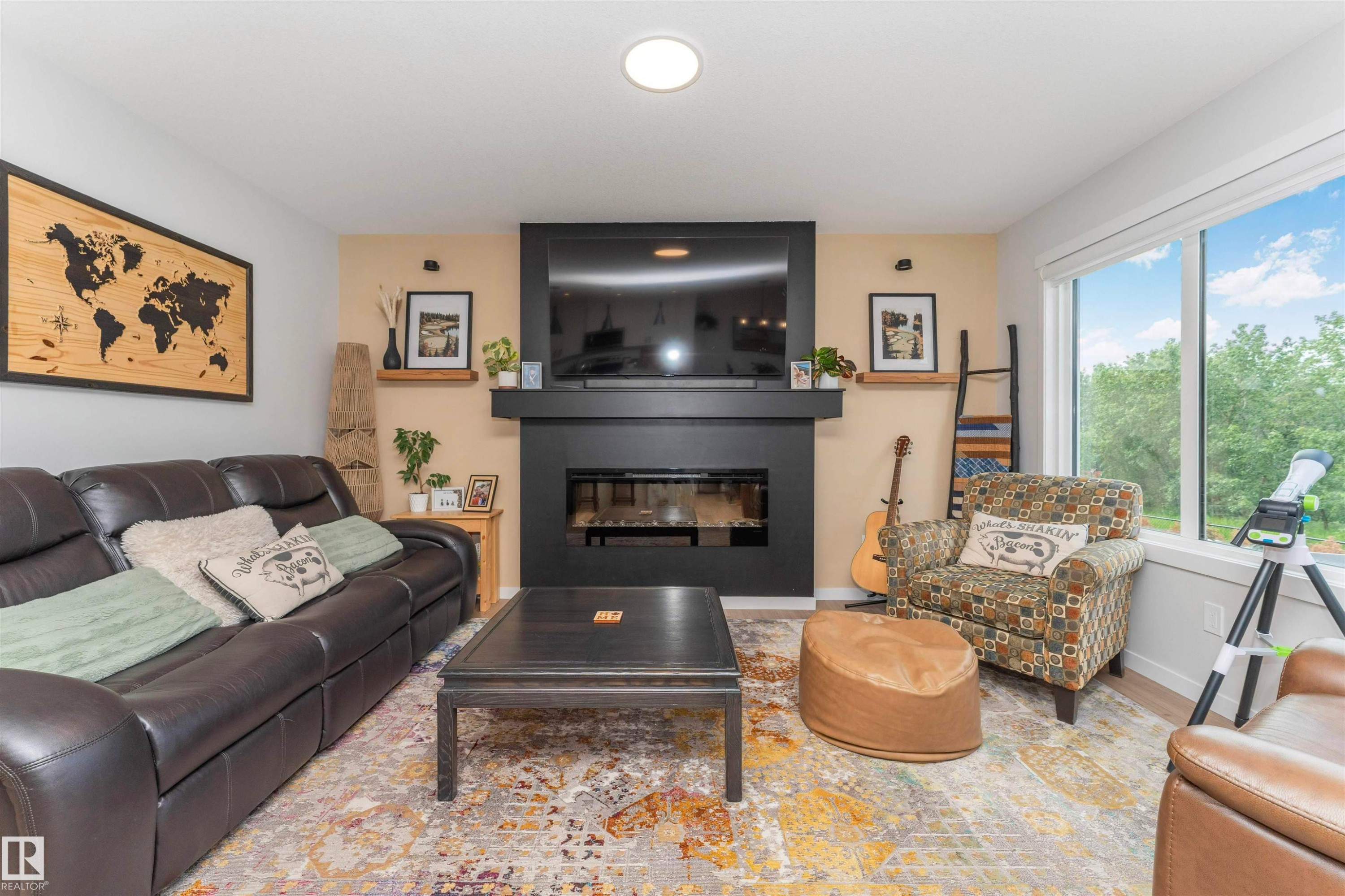 Living area featuring light wood-finish flooring, a modern black fireplace with a mantel, a built-in recessed television, a large window, and recessed ceiling lighting - 102 Horton Way, Ardrossan, AB