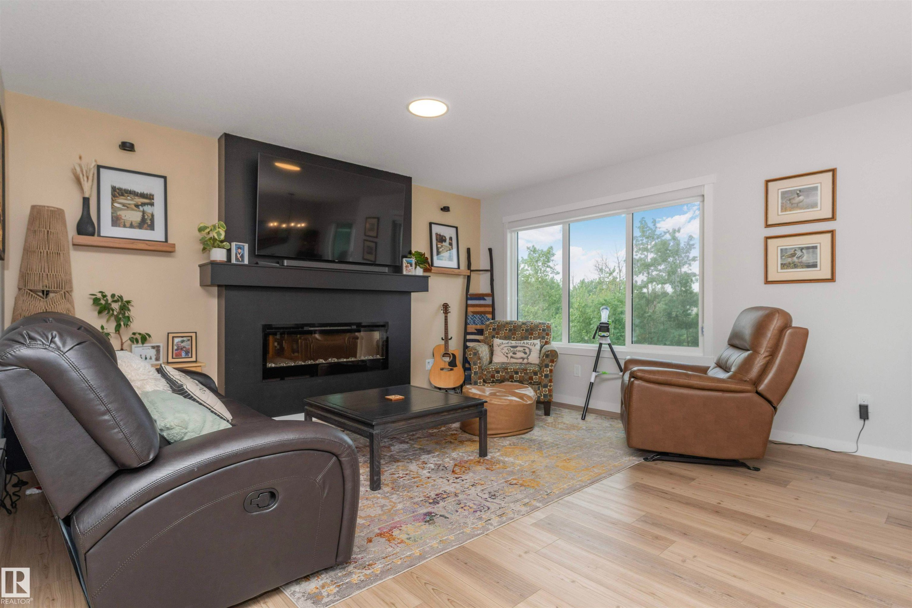 Living area featuring a contemporary linear fireplace with dark mantel, overhead recessed lighting, and wood-finish flooring - 102 Horton Way, Ardrossan, AB