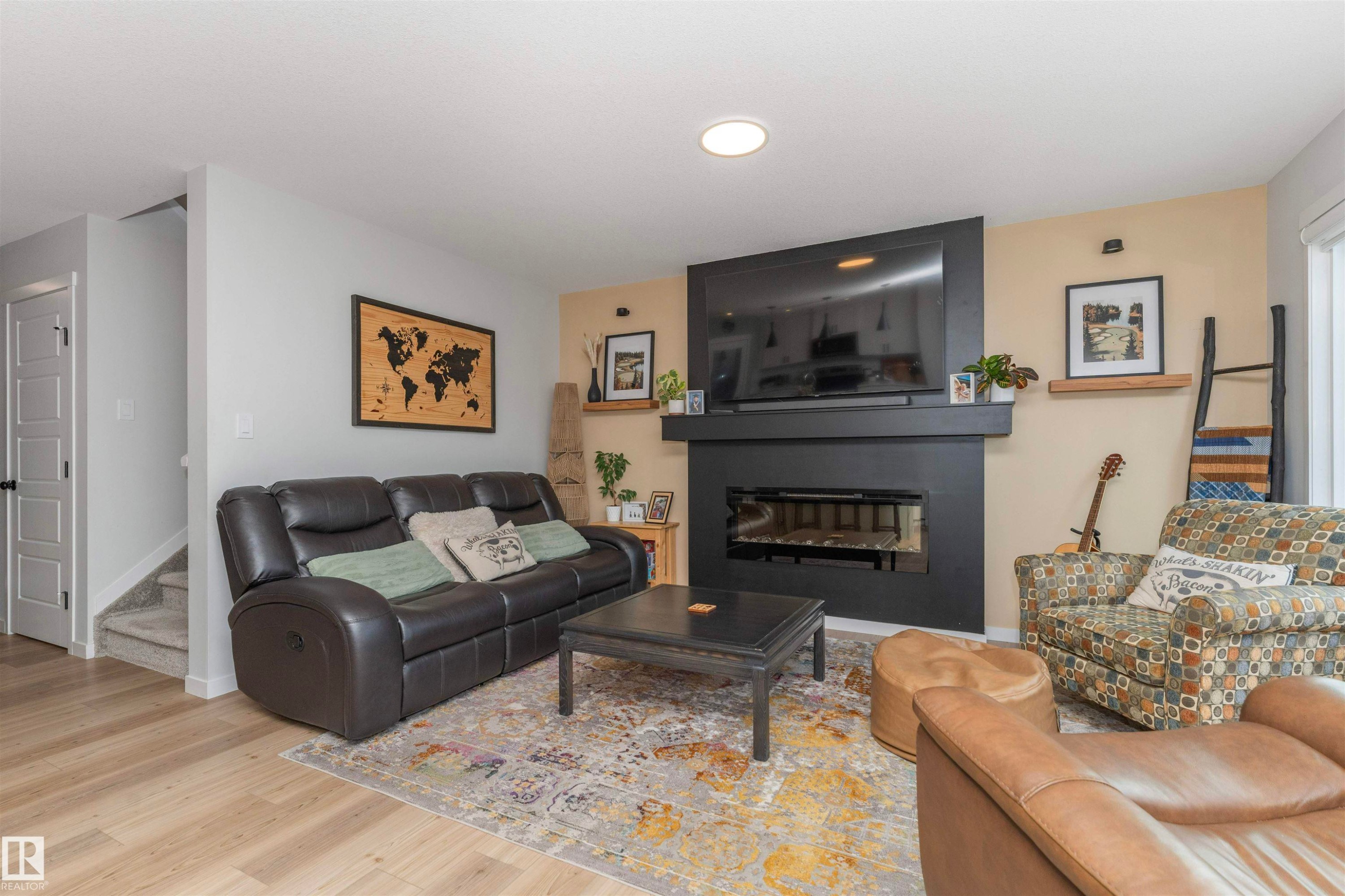Contemporary linear fireplace with a black surround and mantel, light wood-finish flooring, and recessed ceiling lighting - 102 Horton Way, Ardrossan, AB