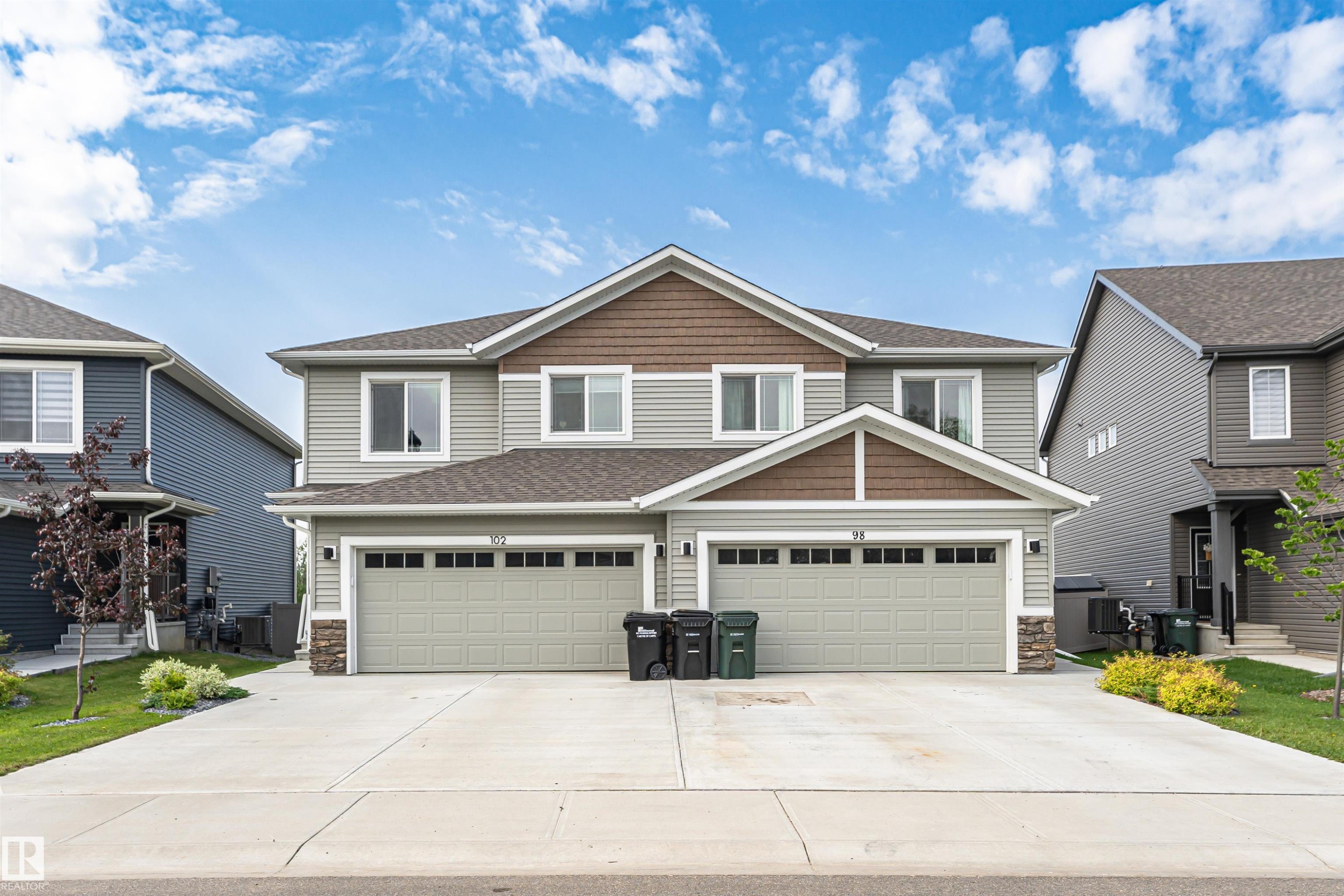 Contemporary duplex featuring light gray siding with brown shake accents - 102 Horton Way, Ardrossan, AB