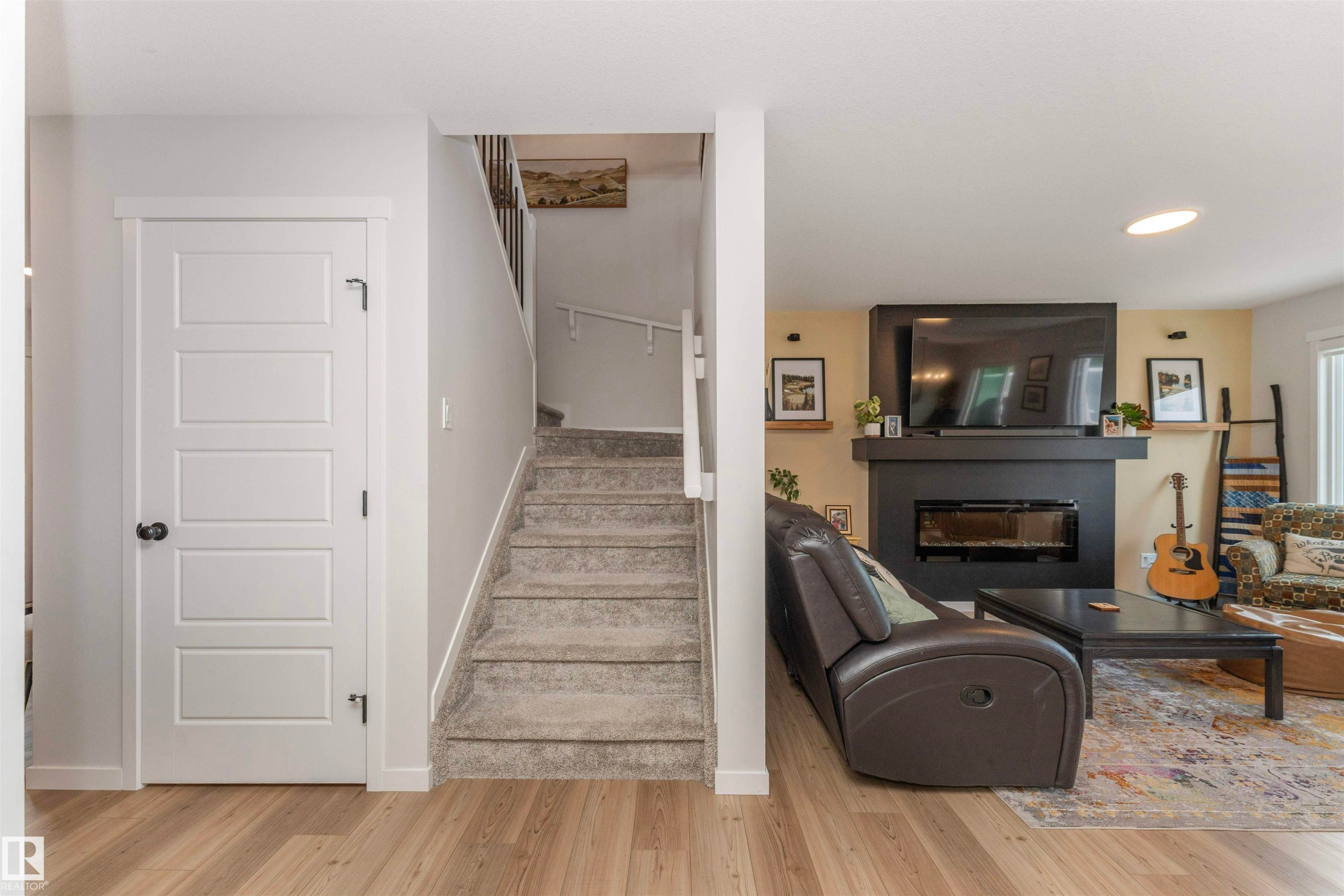 Bright living area featuring wood-finish flooring and a modern fireplace with a black surround - 102 Horton Way, Ardrossan, AB