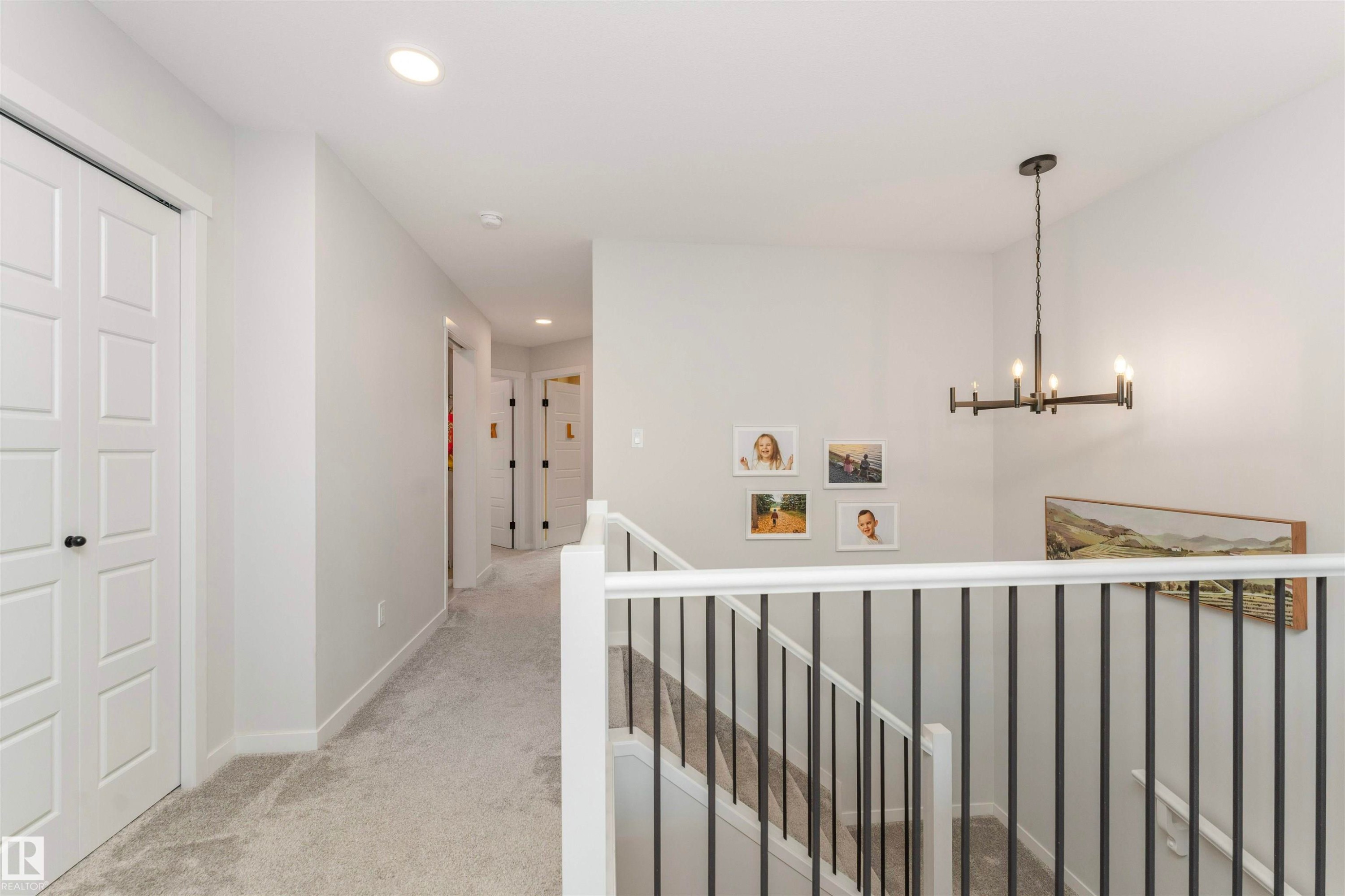 Upper floor landing featuring light gray carpeting, recessed ceiling lighting, a contemporary black metal chandelier, and white paneled doors - 102 Horton Way, Ardrossan, AB