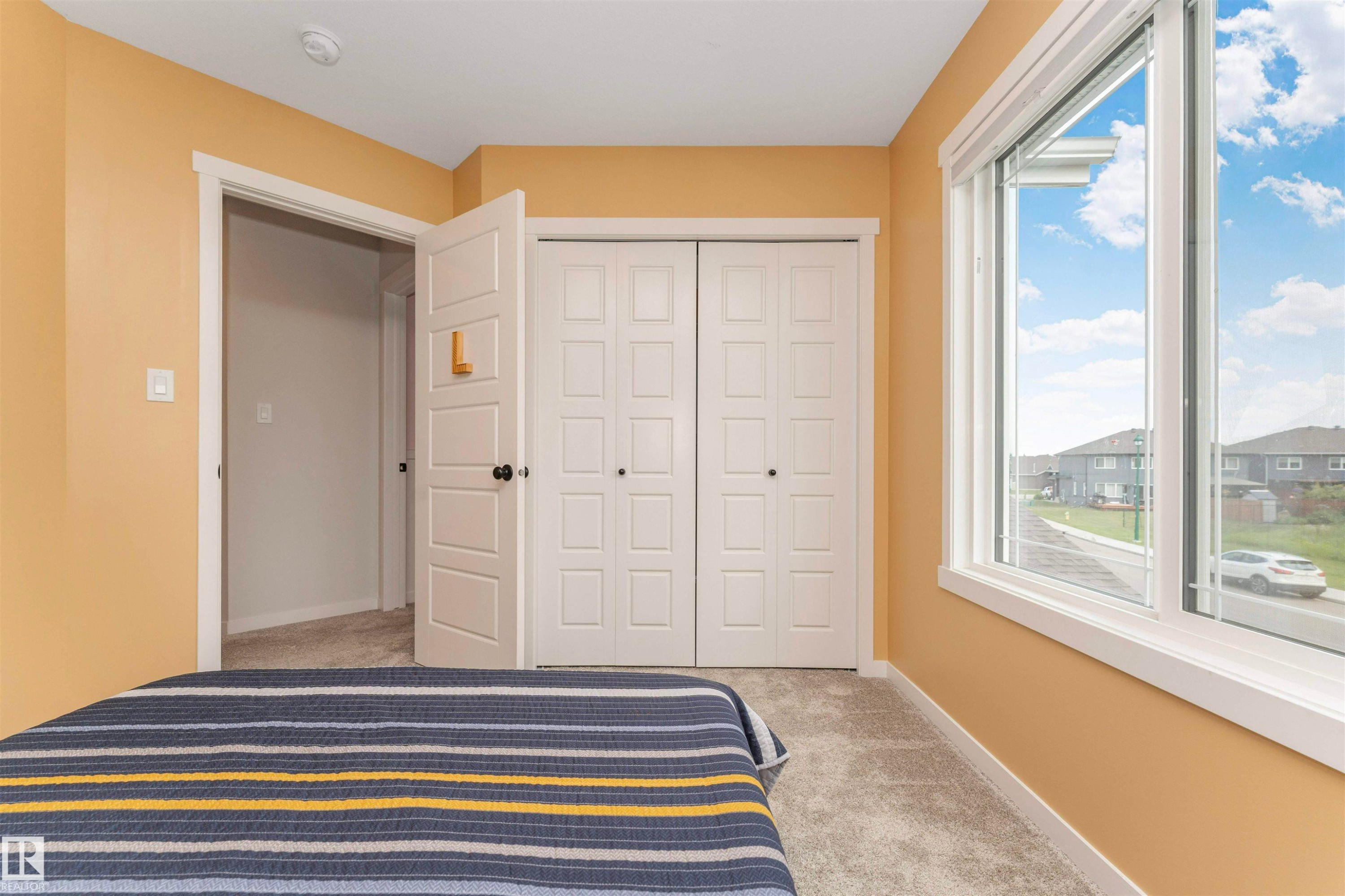 Bright interior featuring a large window with white trim, soft carpeting, and a built-in closet with bifold doors - 102 Horton Way, Ardrossan, AB