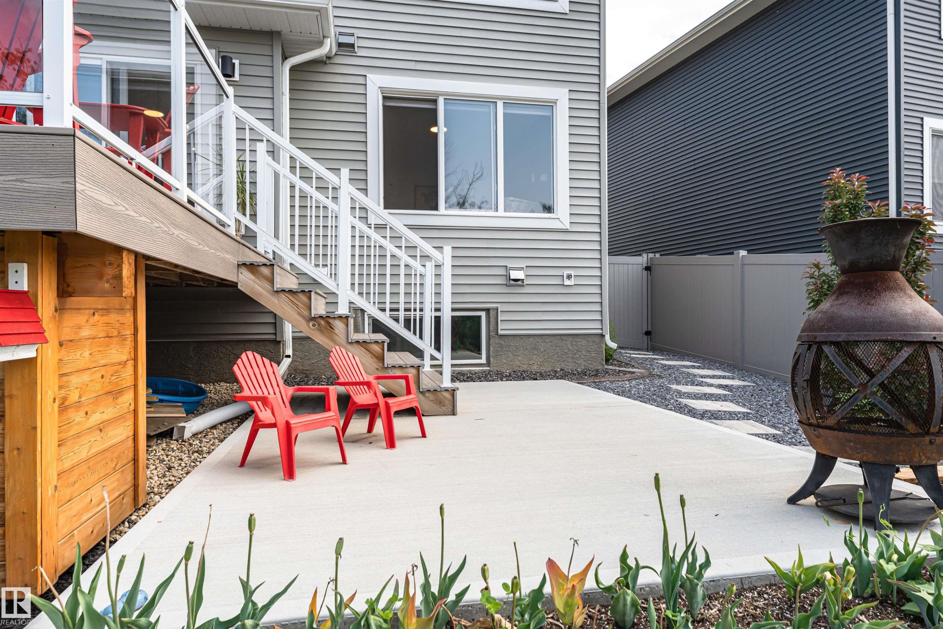 Concrete patio featuring a decorative fire pit, gravel pathway with stepping stones, and a multi-level deck with white railings - 102 Horton Way, Ardrossan, AB