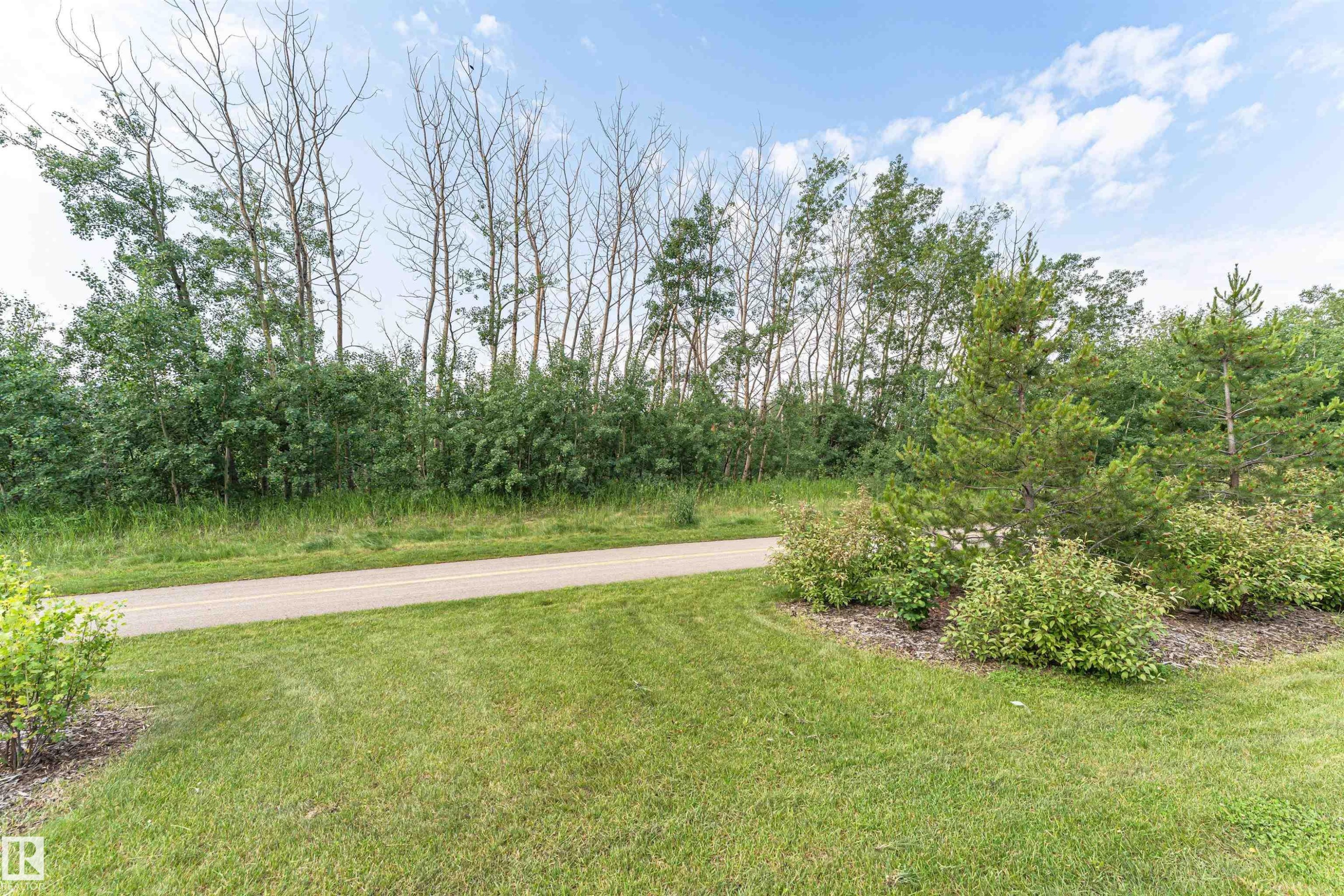 Manicured lawn area with a paved pathway, bordered by mature trees and shrubs - 102 Horton Way, Ardrossan, AB