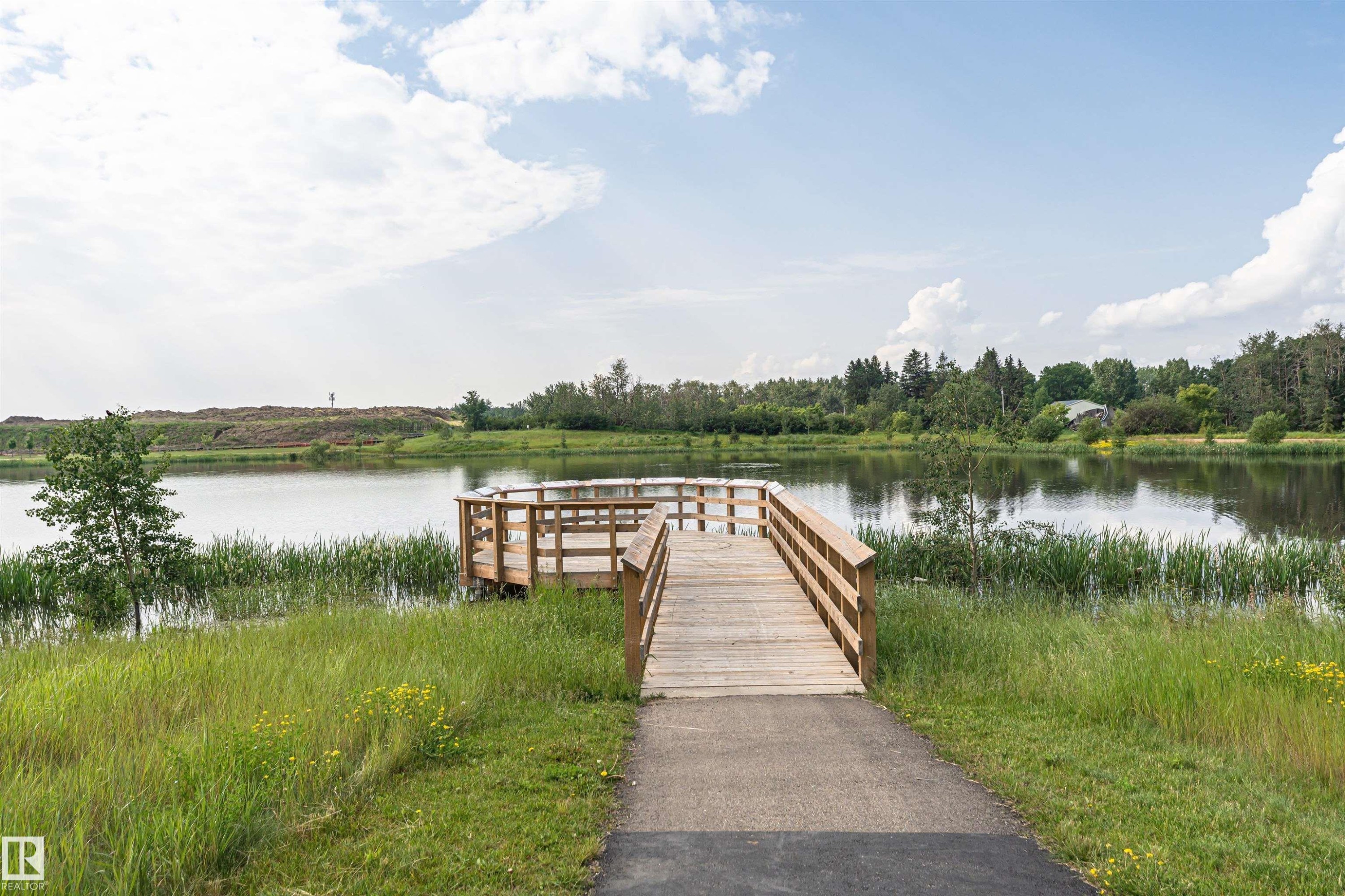 Waterfront property featuring a wooden dock, a paved path, mature trees, and natural landscaping - 102 Horton Way, Ardrossan, AB