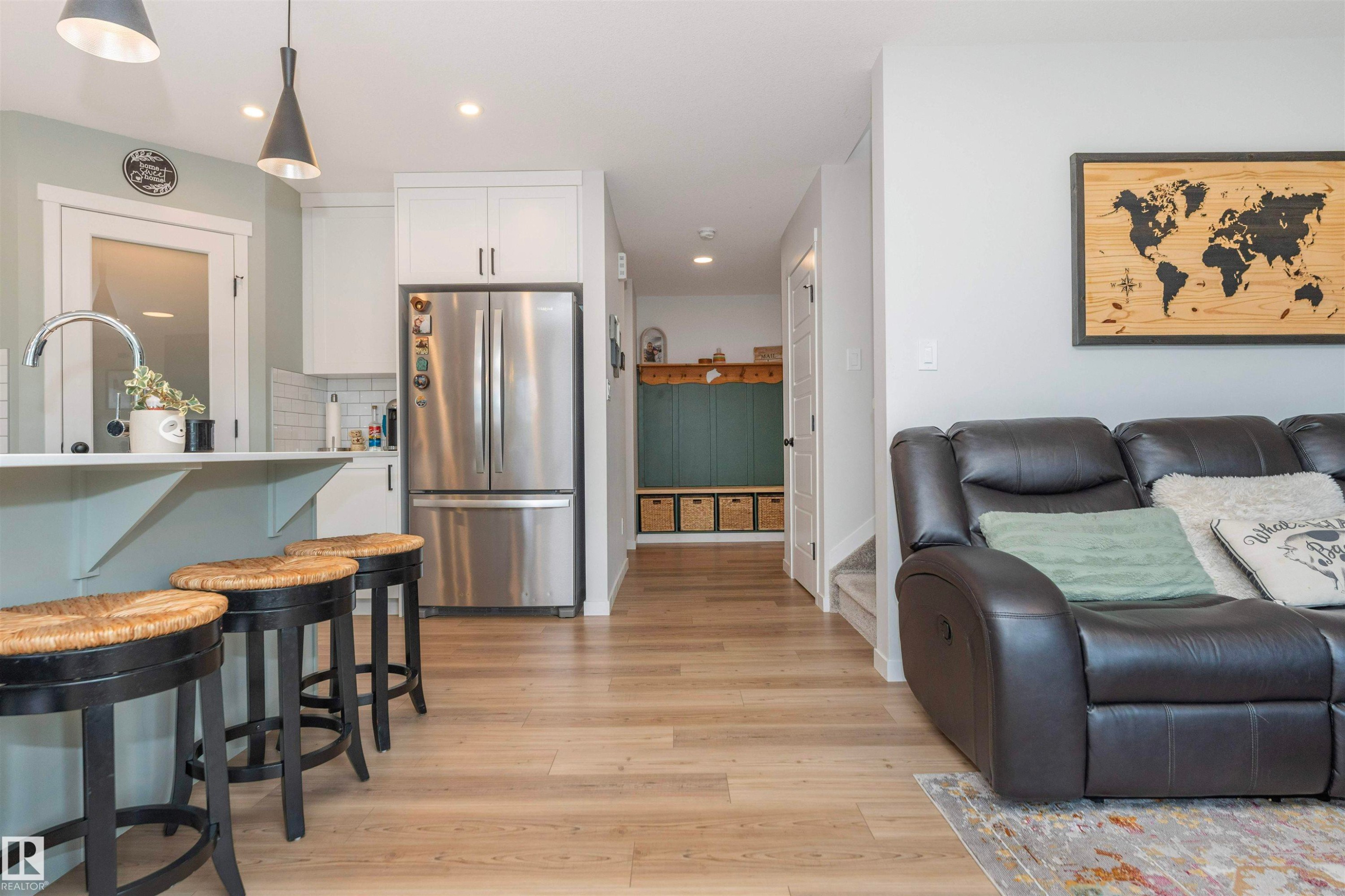 Open-concept living space featuring wood-finish flooring, a kitchen island with seating, white cabinetry, stainless steel appliances, and a built-in hallway bench - 102 Horton Way, Ardrossan, AB