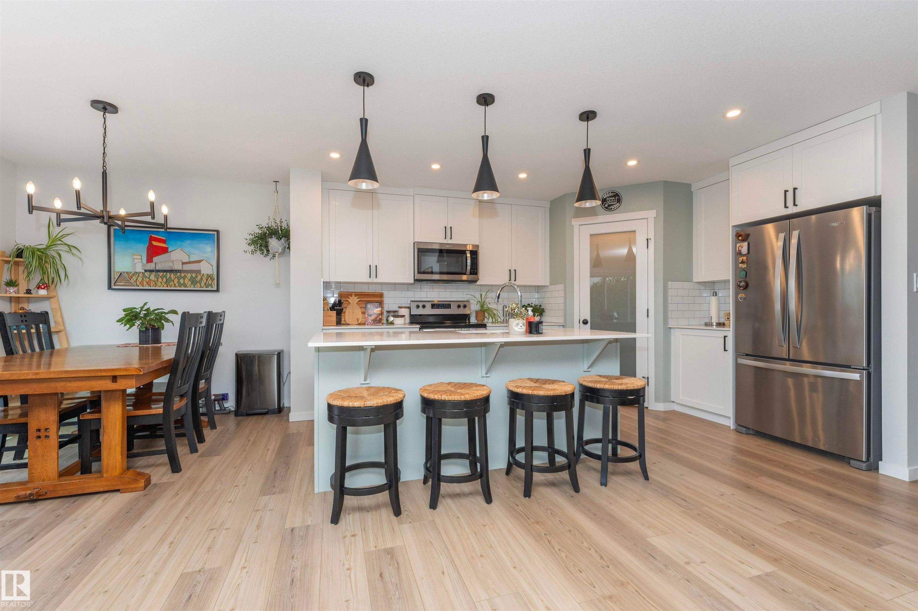 Open-concept kitchen featuring an island with seating, stainless steel appliances, white cabinetry, subway tile backsplash, and light wood-finish flooring - 102 Horton Way, Ardrossan, AB