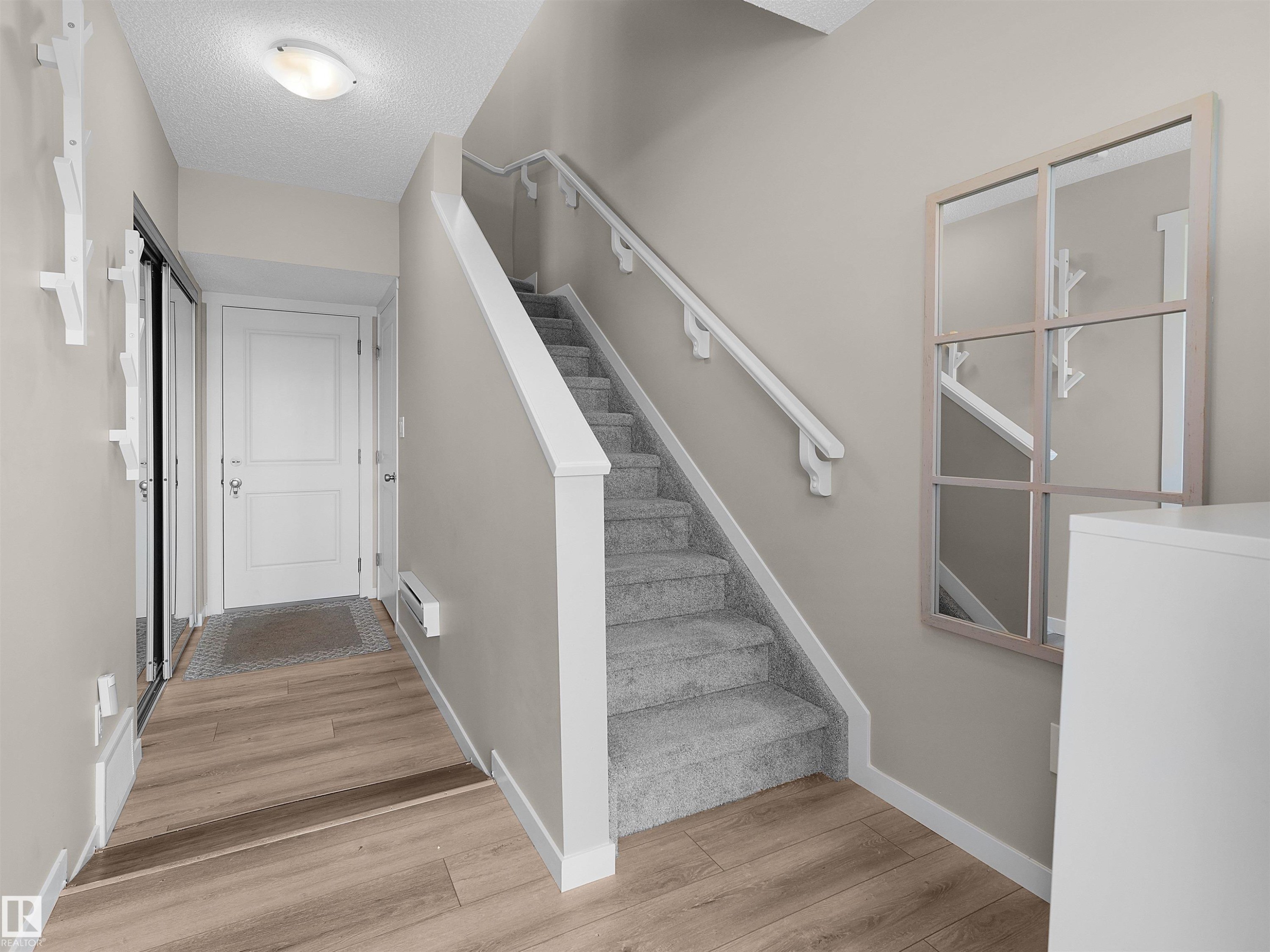 Entryway featuring wood-finish flooring, a carpeted staircase with white handrails, and a modern overhead light fixture - #49 17832 78 St Nw, Edmonton, AB - Indoor Photo Showing Other Room