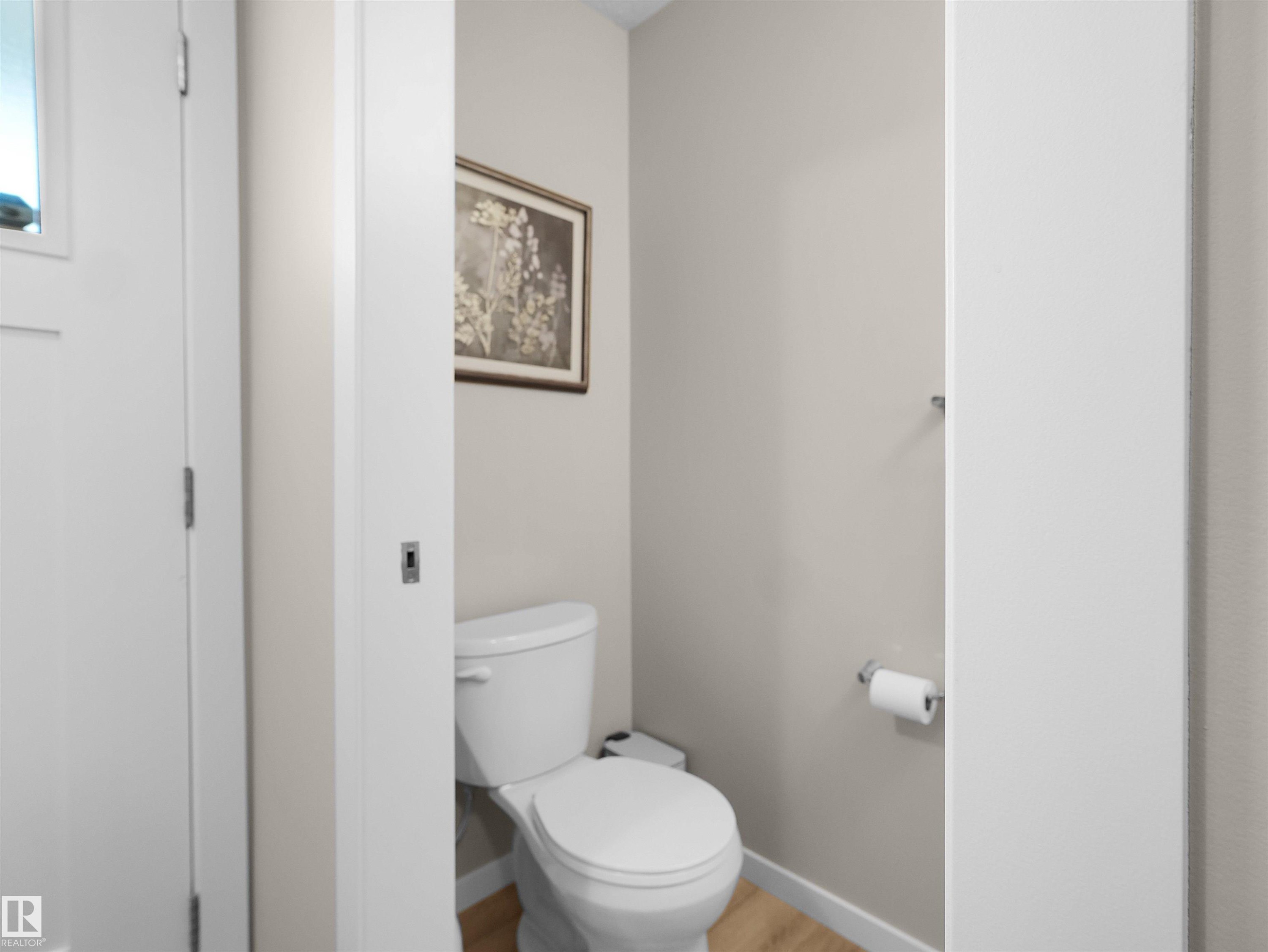 White toilet with light beige wall paint, wood-finish flooring, and a chrome towel bar - #49 17832 78 St Nw, Edmonton, AB - Indoor Photo Showing Bathroom