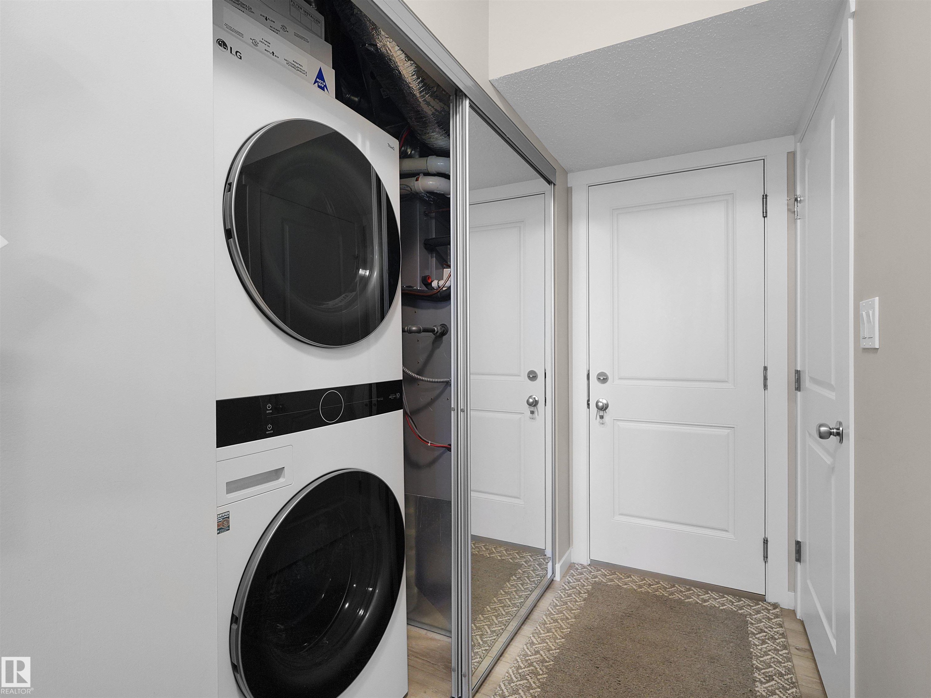 Integrated laundry closet featuring a stacked washer and dryer, mirrored closet doors, and panel doors with chrome hardware - #49 17832 78 St Nw, Edmonton, AB - Indoor Photo Showing Laundry Room