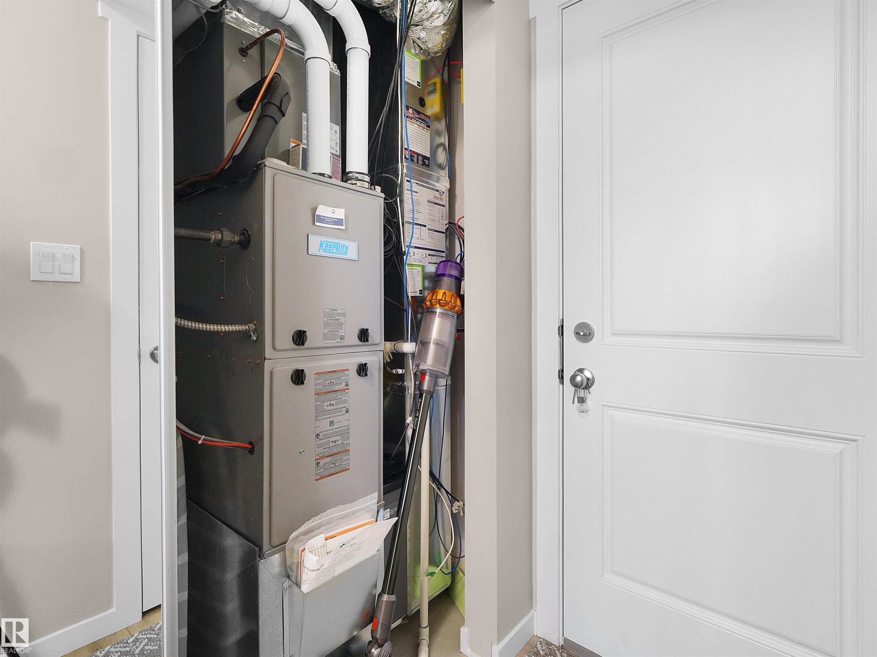 Utility closet featuring a central HVAC system with visible ductwork and piping, and a white paneled door - #49 17832 78 St Nw, Edmonton, AB - Indoor Photo Showing Basement