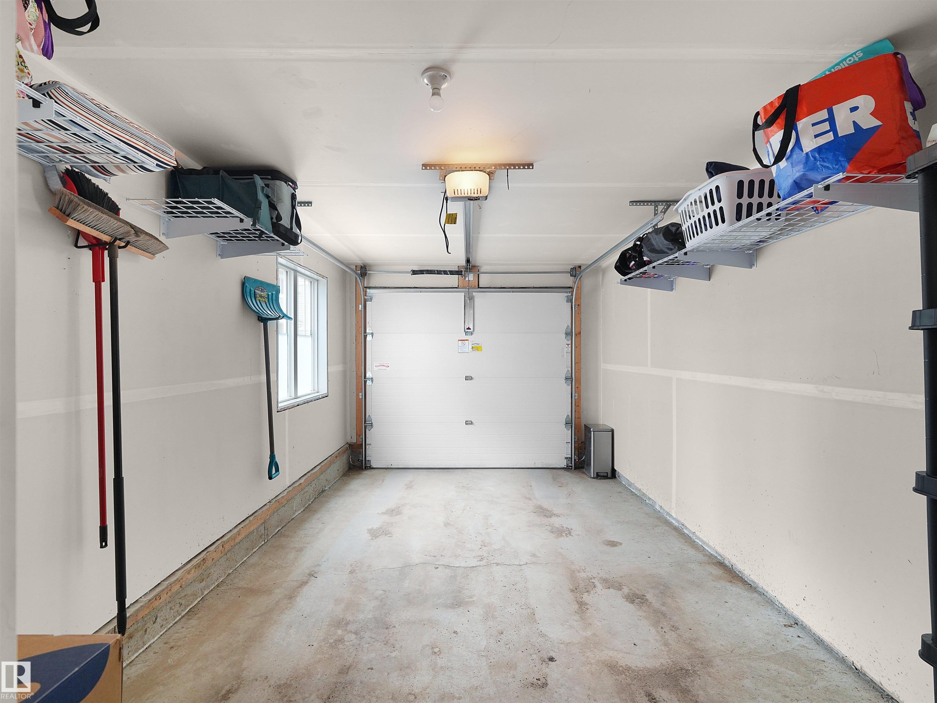 Single-car garage with a concrete floor, equipped with an automatic garage door opener, overhead storage racks, and a window for natural light - #49 17832 78 St Nw, Edmonton, AB - Indoor Photo Showing Garage