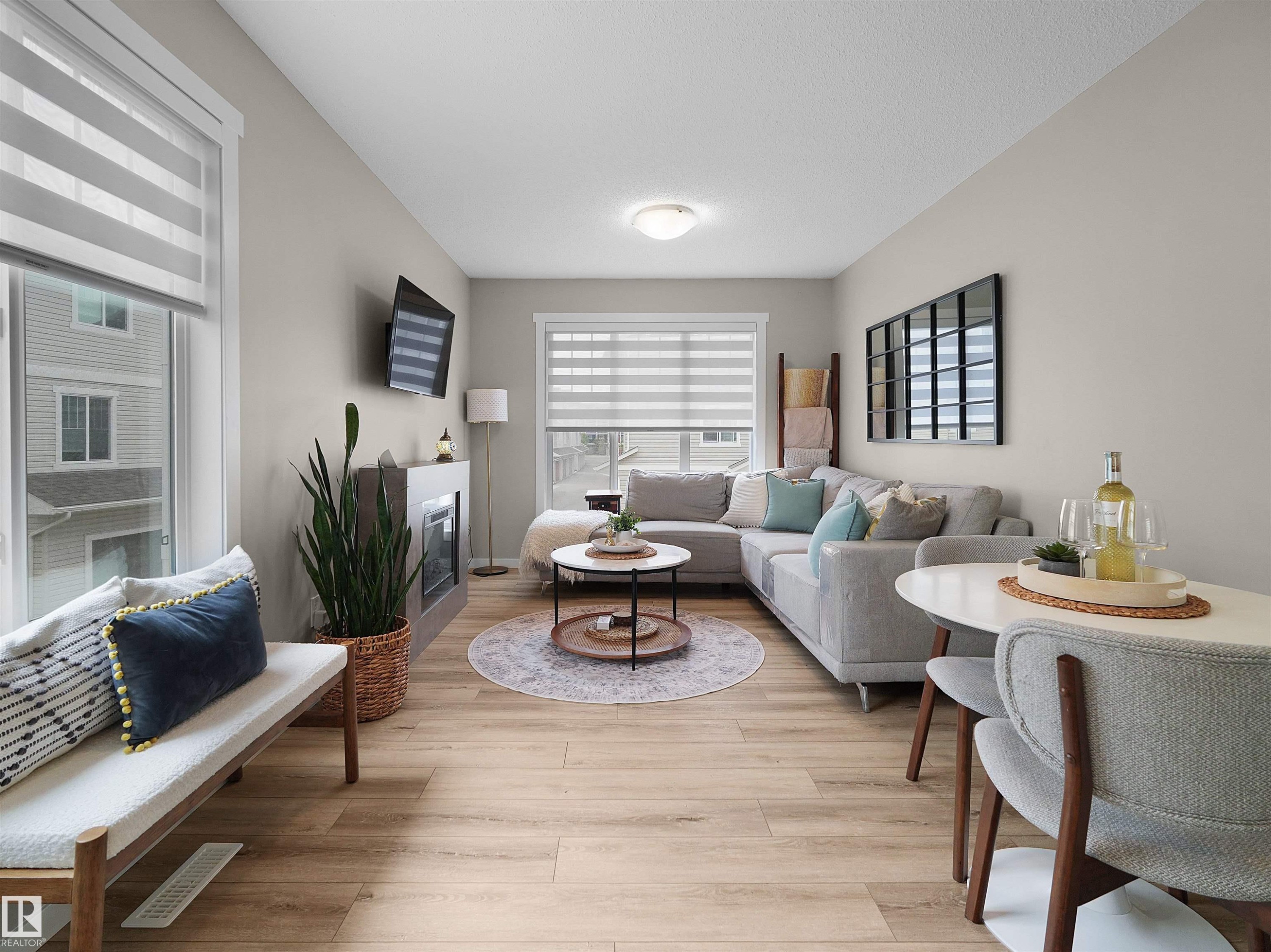Open-concept living area featuring light wood-finish flooring, a contemporary fireplace, and a large window with privacy blinds - #49 17832 78 St Nw, Edmonton, AB - Indoor Photo Showing Living Room