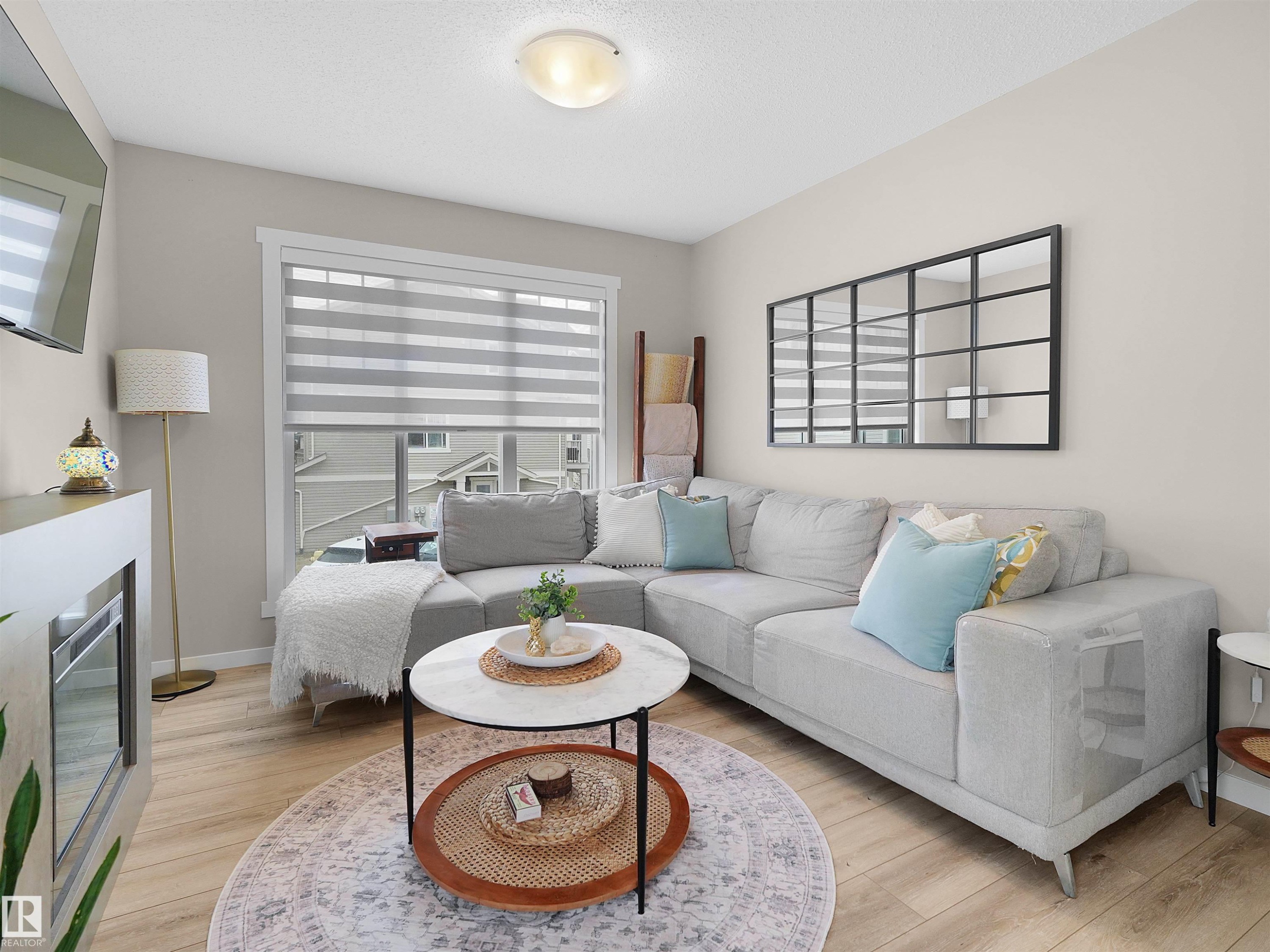 Living room featuring light wood-finish flooring, a large window with privacy blinds, and a built-in electric fireplace - #49 17832 78 St Nw, Edmonton, AB - Indoor Photo Showing Living Room