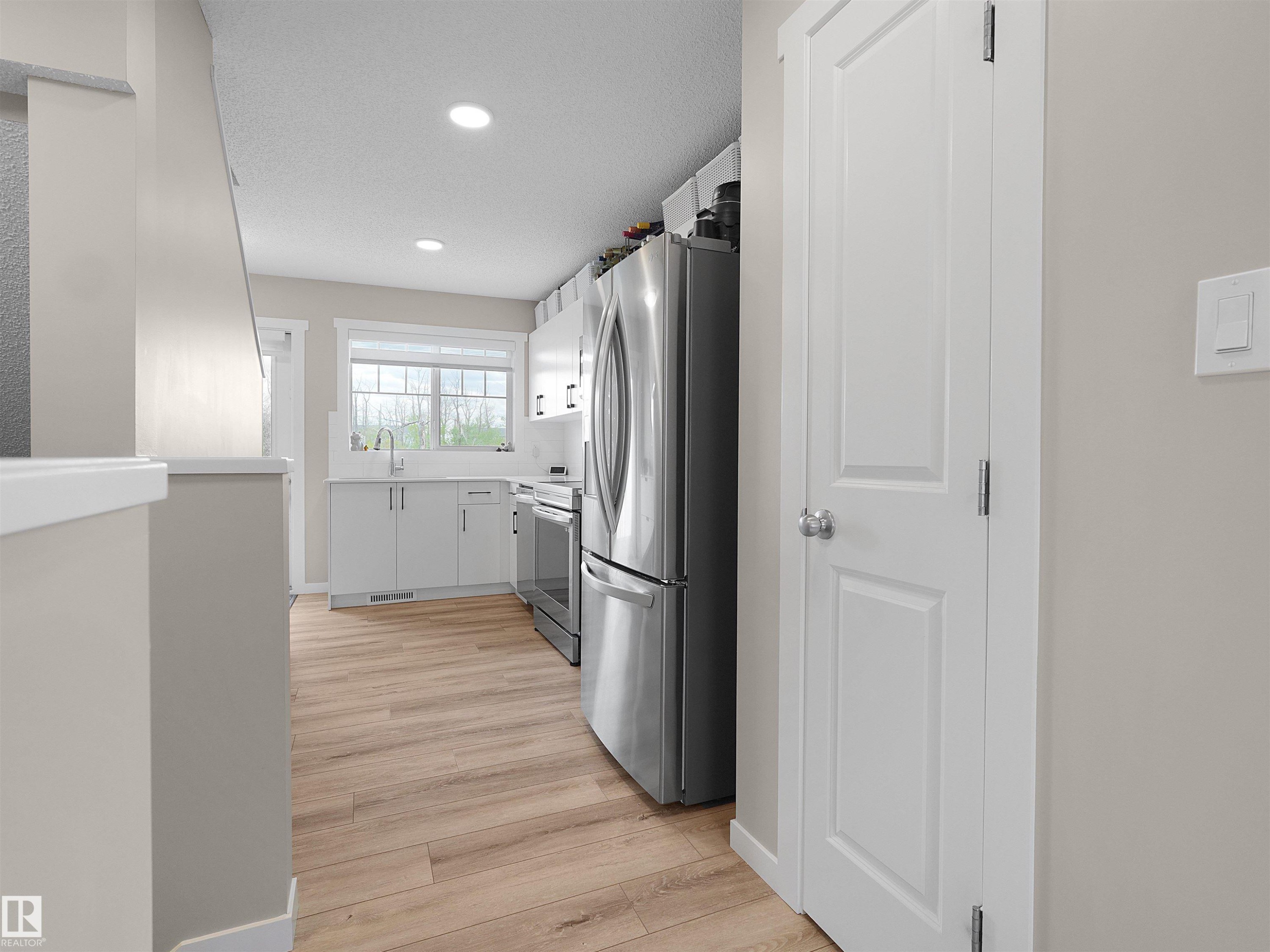 Light wood-finish flooring extending into the kitchen with recessed ceiling lighting, a window over the sink, and stainless steel appliances - #49 17832 78 St Nw, Edmonton, AB - Indoor
