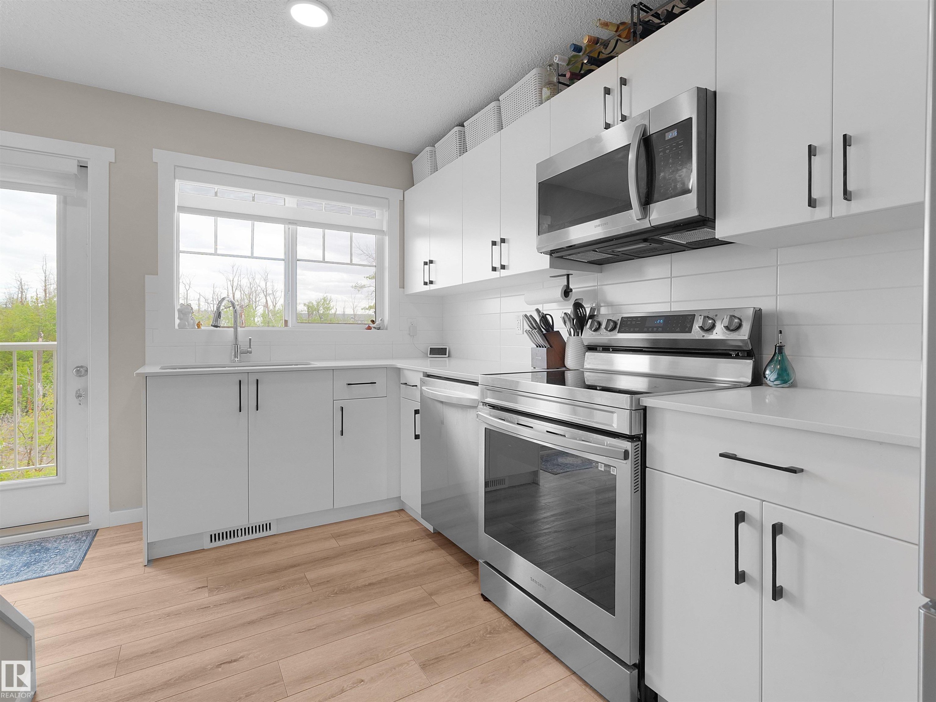 Modern kitchen with white cabinetry and wood-finish flooring - #49 17832 78 St Nw, Edmonton, AB - Indoor Photo Showing Kitchen