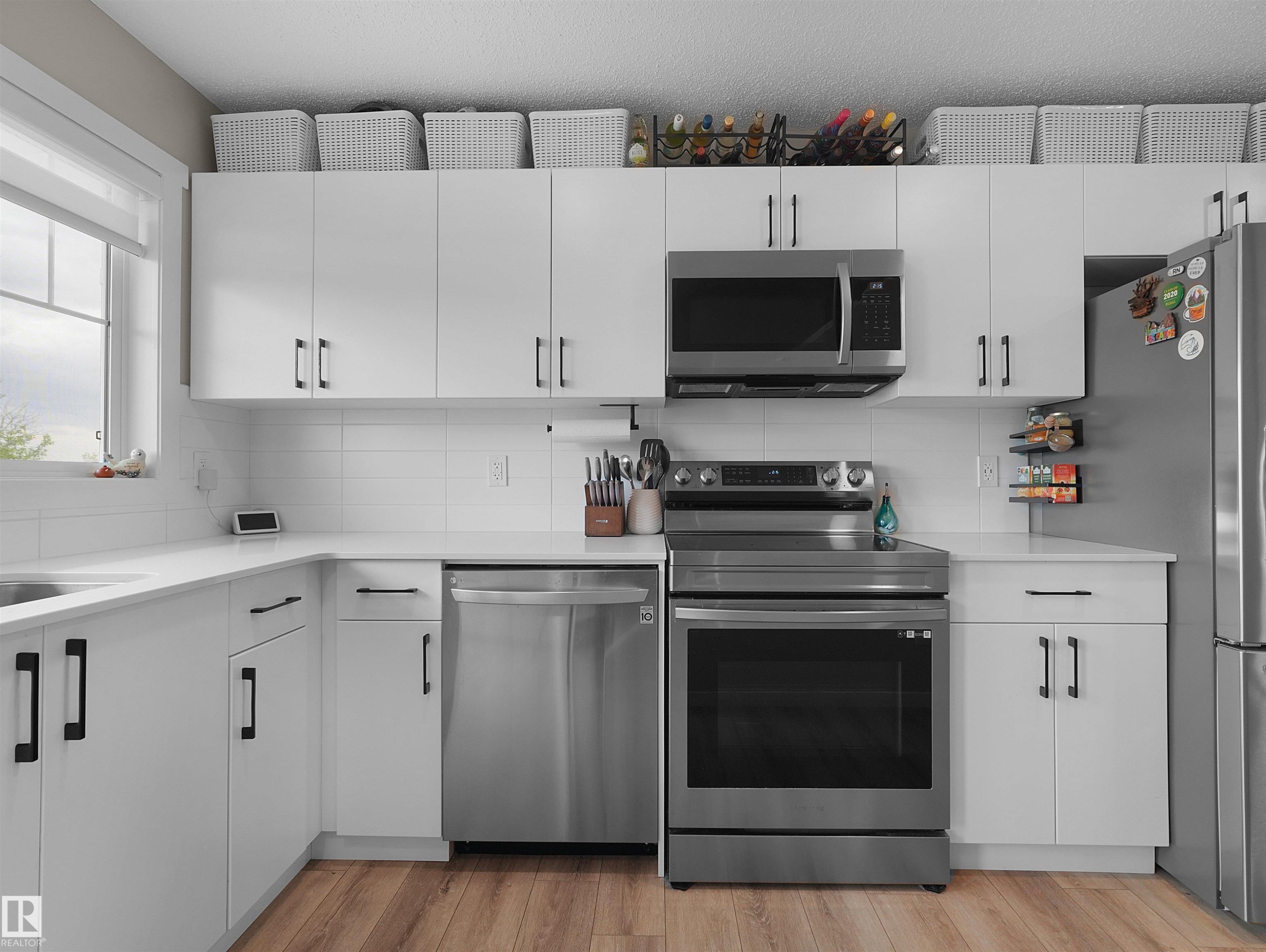 Modern kitchen featuring white cabinetry, quartz-finish countertops, stainless steel appliances, a white tile backsplash, and wood-finish flooring - #49 17832 78 St Nw, Edmonton, AB - Indoor Photo Showing Kitchen With Upgraded Kitchen