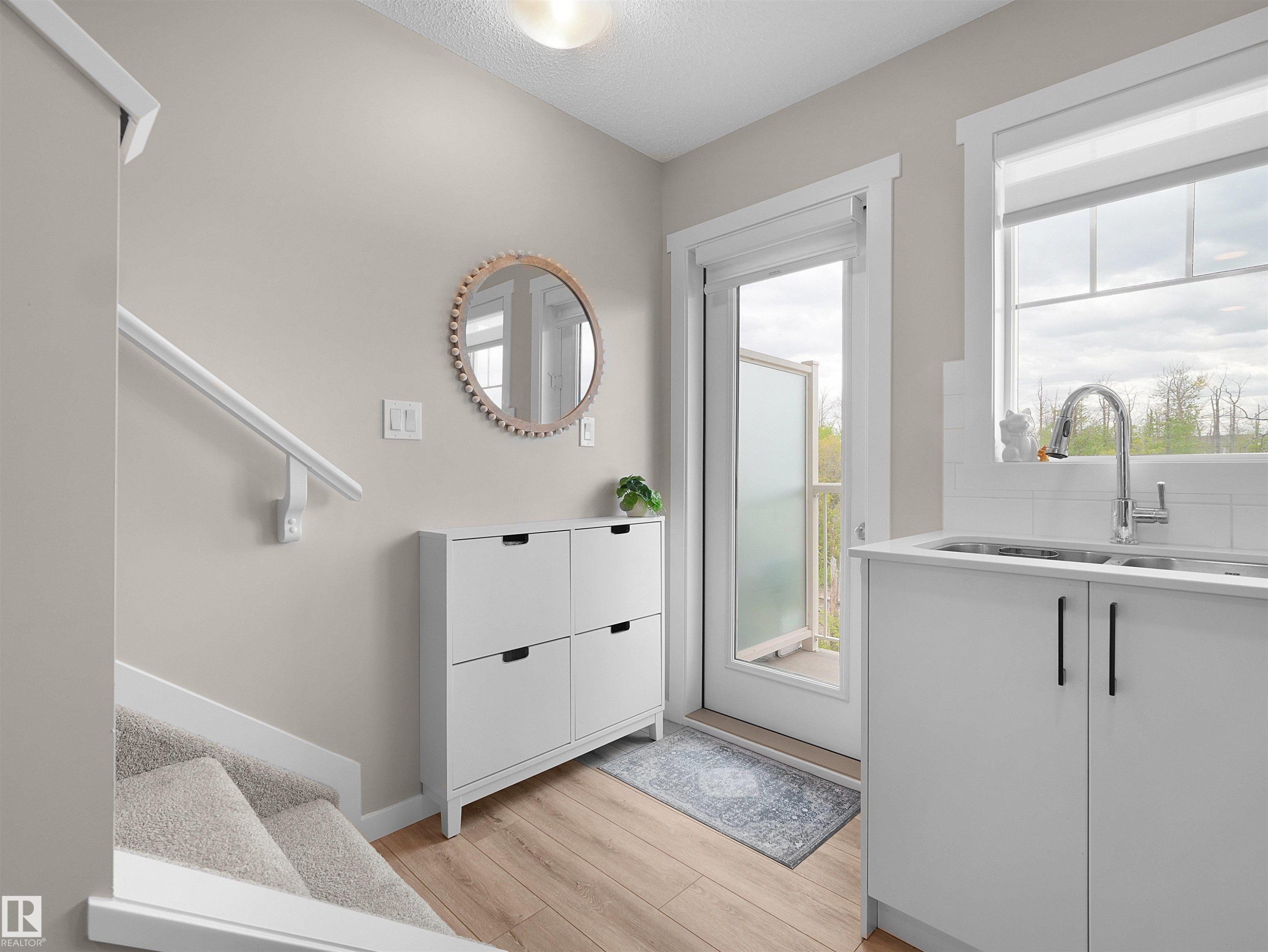 Entryway featuring wood-finish flooring, a carpeted staircase with white railing, and a functional sink area with white cabinetry - #49 17832 78 St Nw, Edmonton, AB - Indoor
