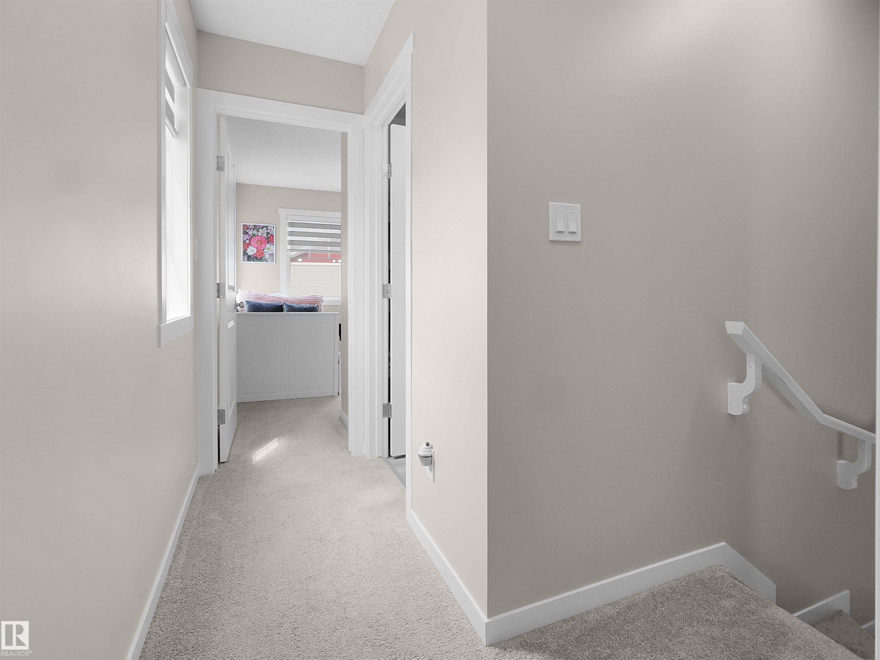 Hallway featuring light neutral wall paint, light-colored carpeting, white trim, and a white handrail leading to a lower level - #49 17832 78 St Nw, Edmonton, AB - Indoor Photo Showing Other Room