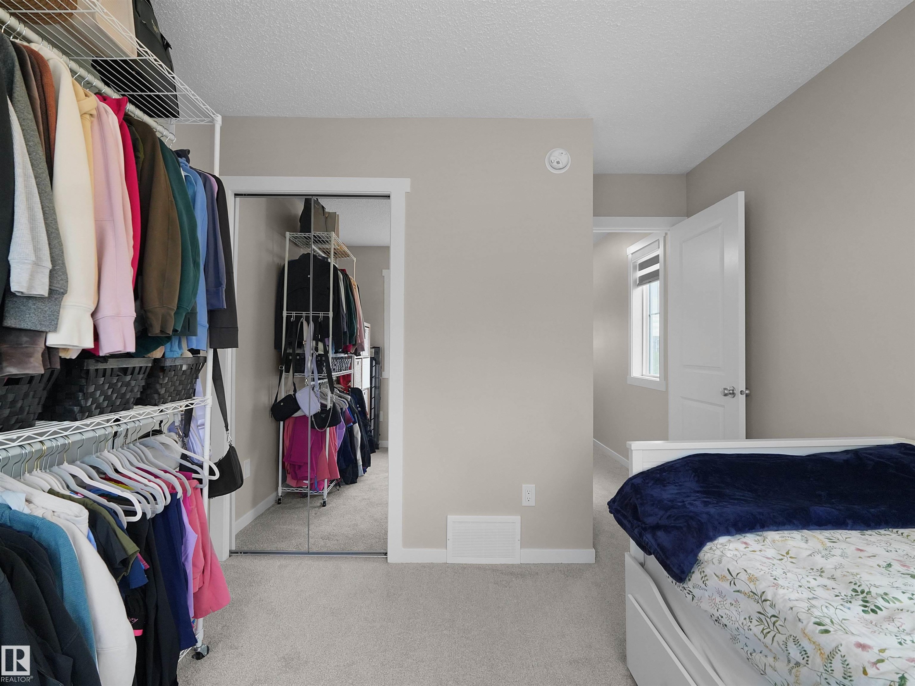 Bedroom featuring plush carpet flooring, neutral wall tones, a built-in closet system with wire shelving, and a mirrored sliding closet door - #49 17832 78 St Nw, Edmonton, AB - Indoor With Storage