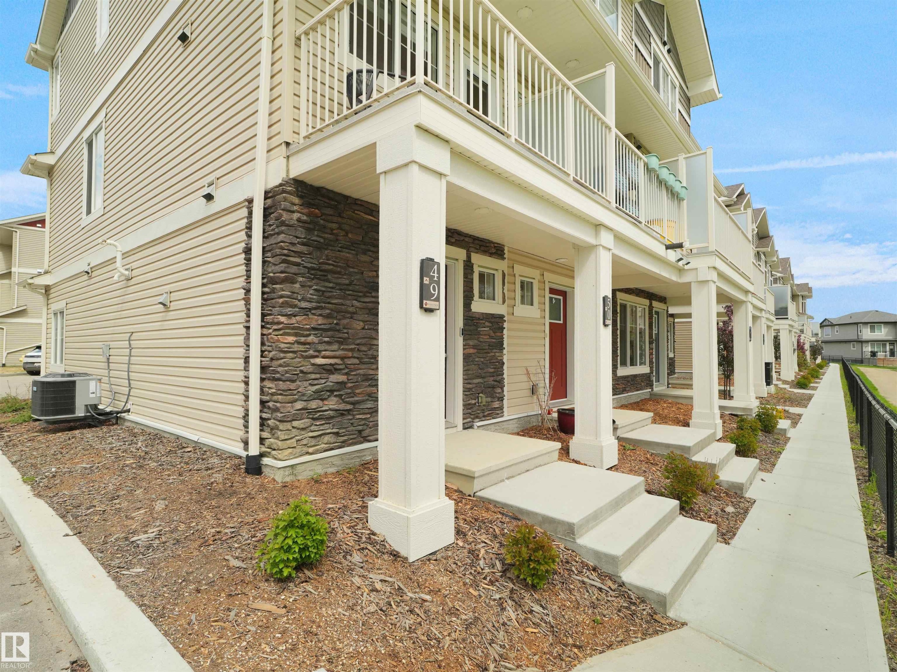 Townhome exterior with light beige horizontal siding, a stacked stone accent wall, and a red entry door - #49 17832 78 St Nw, Edmonton, AB - Outdoor With Balcony