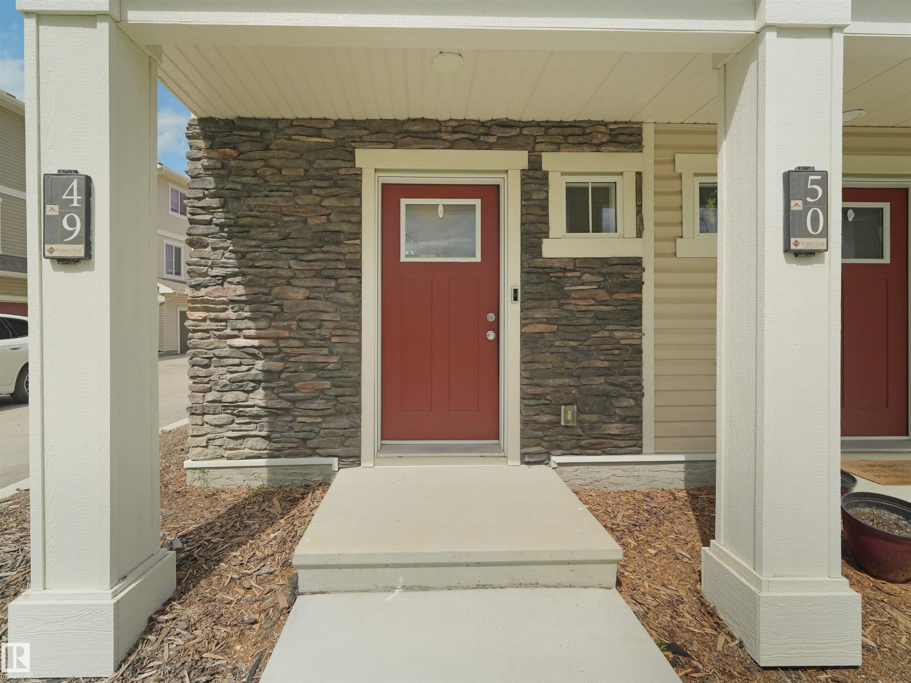 Entryway featuring a red paneled door with window, stone veneer accent, and concrete steps - #49 17832 78 St Nw, Edmonton, AB - Outdoor With Exterior