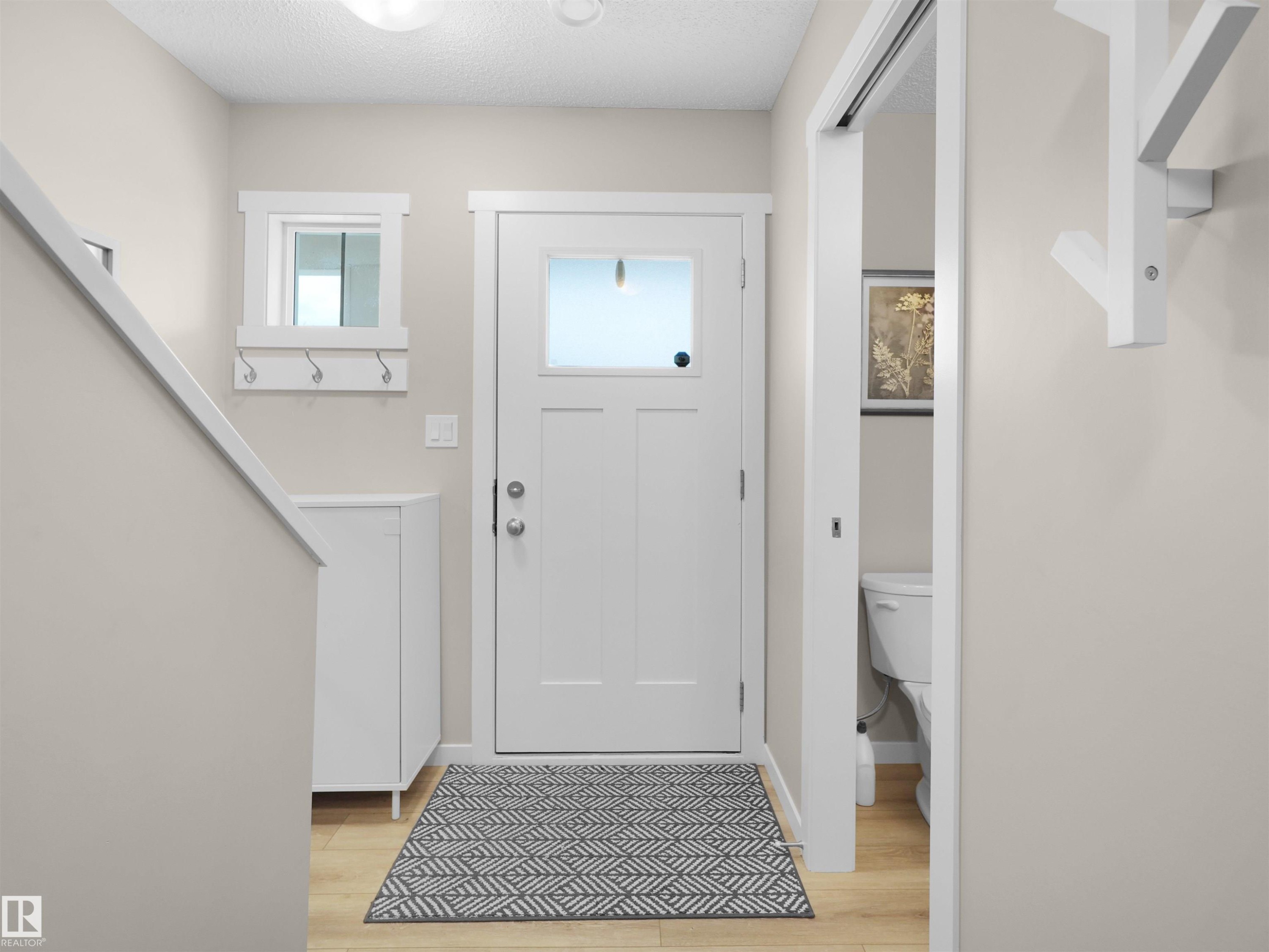 Entryway featuring wood-finish flooring, a white paneled door with frosted glass, and a built-in wall-mounted coat rack - #49 17832 78 St Nw, Edmonton, AB - Indoor Photo Showing Other Room