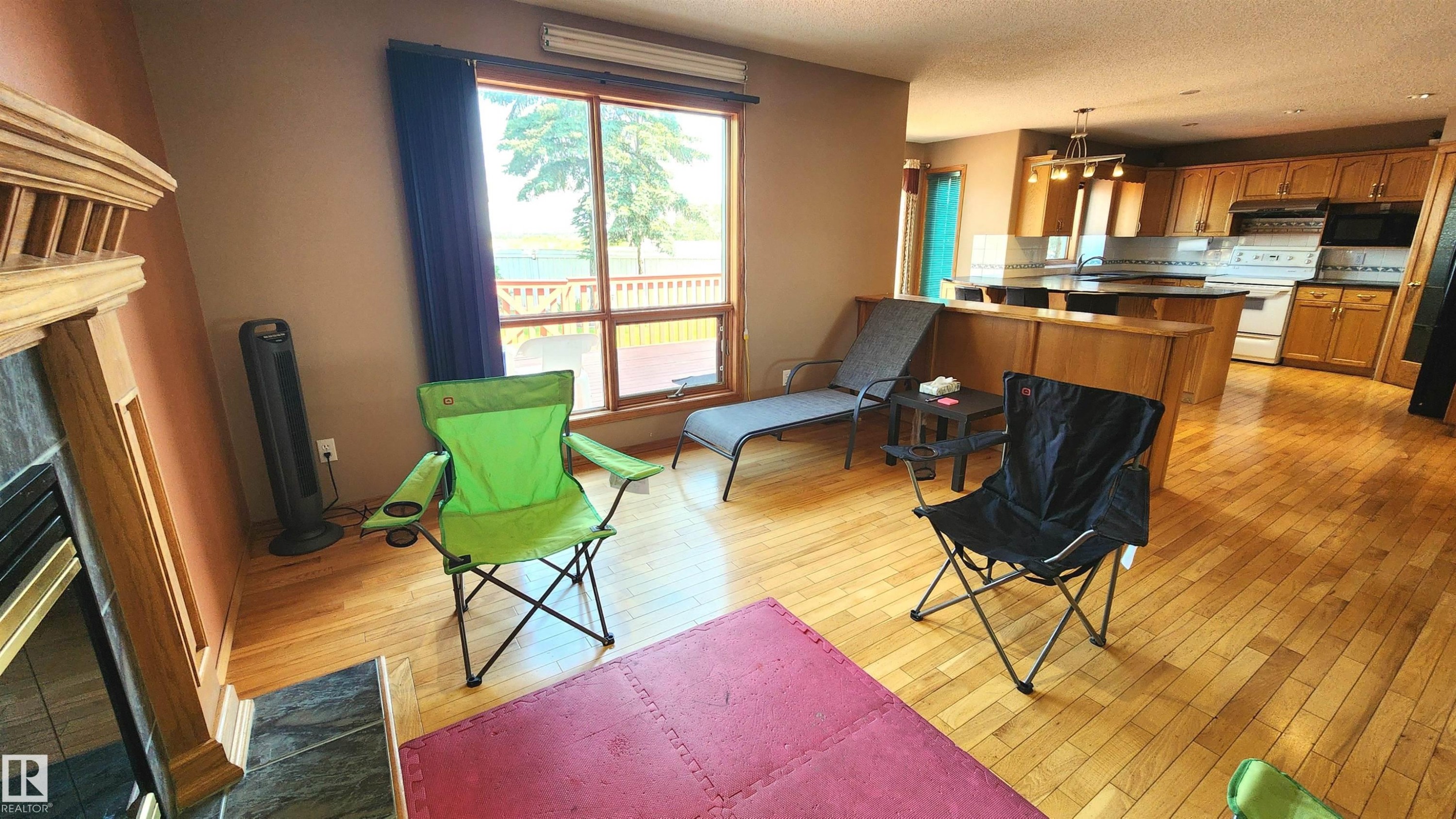 Open-concept living space with wood-finish flooring, a stone-faced fireplace with a wood mantle, and a large window - 2708 44A Avenue, Edmonton, AB