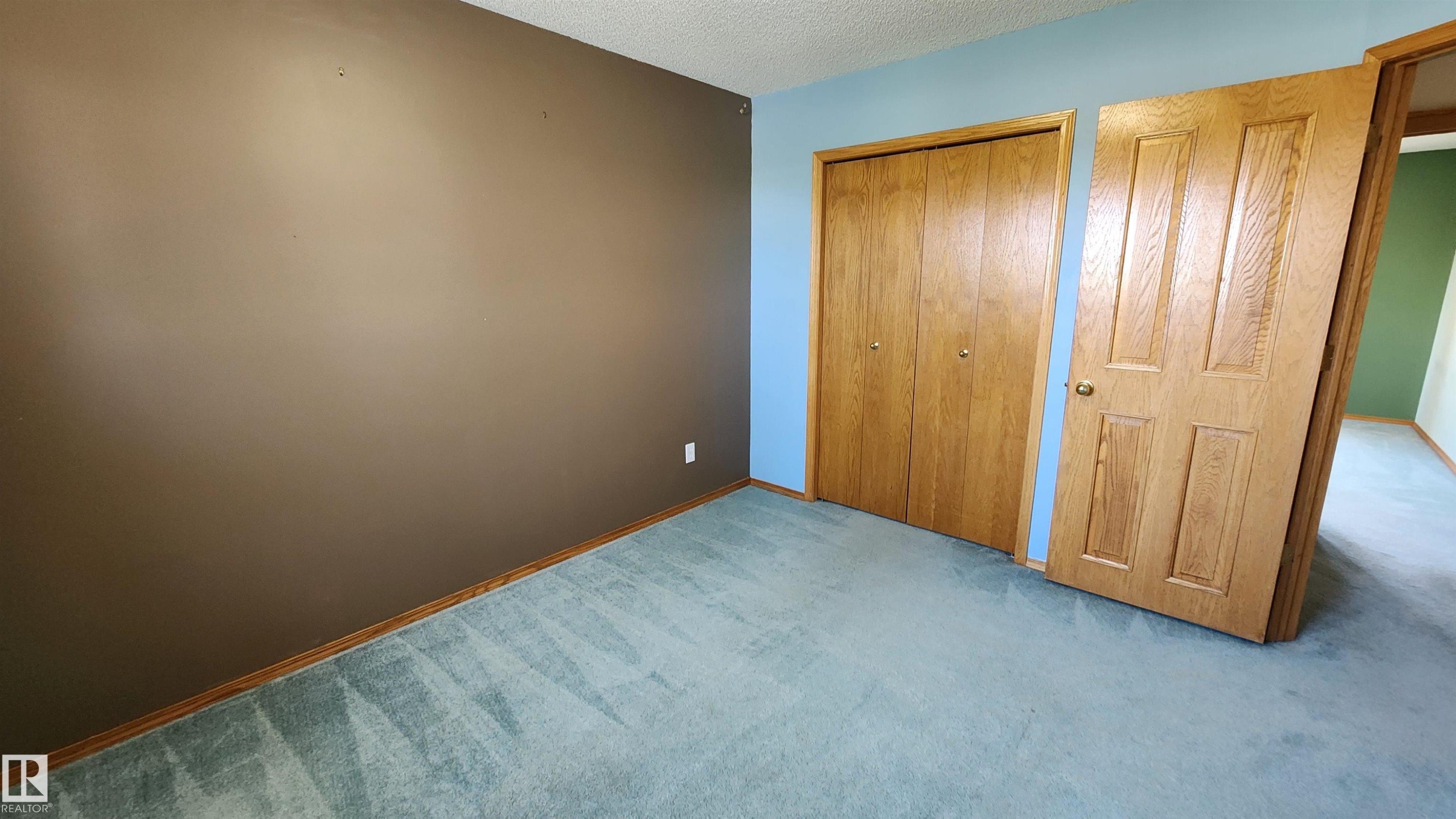 Bedroom space featuring light blue and brown painted walls, light blue carpeting, wood-paneled bi-fold closet doors, and wood-paneled interior doors - 2708 44A Avenue, Edmonton, AB