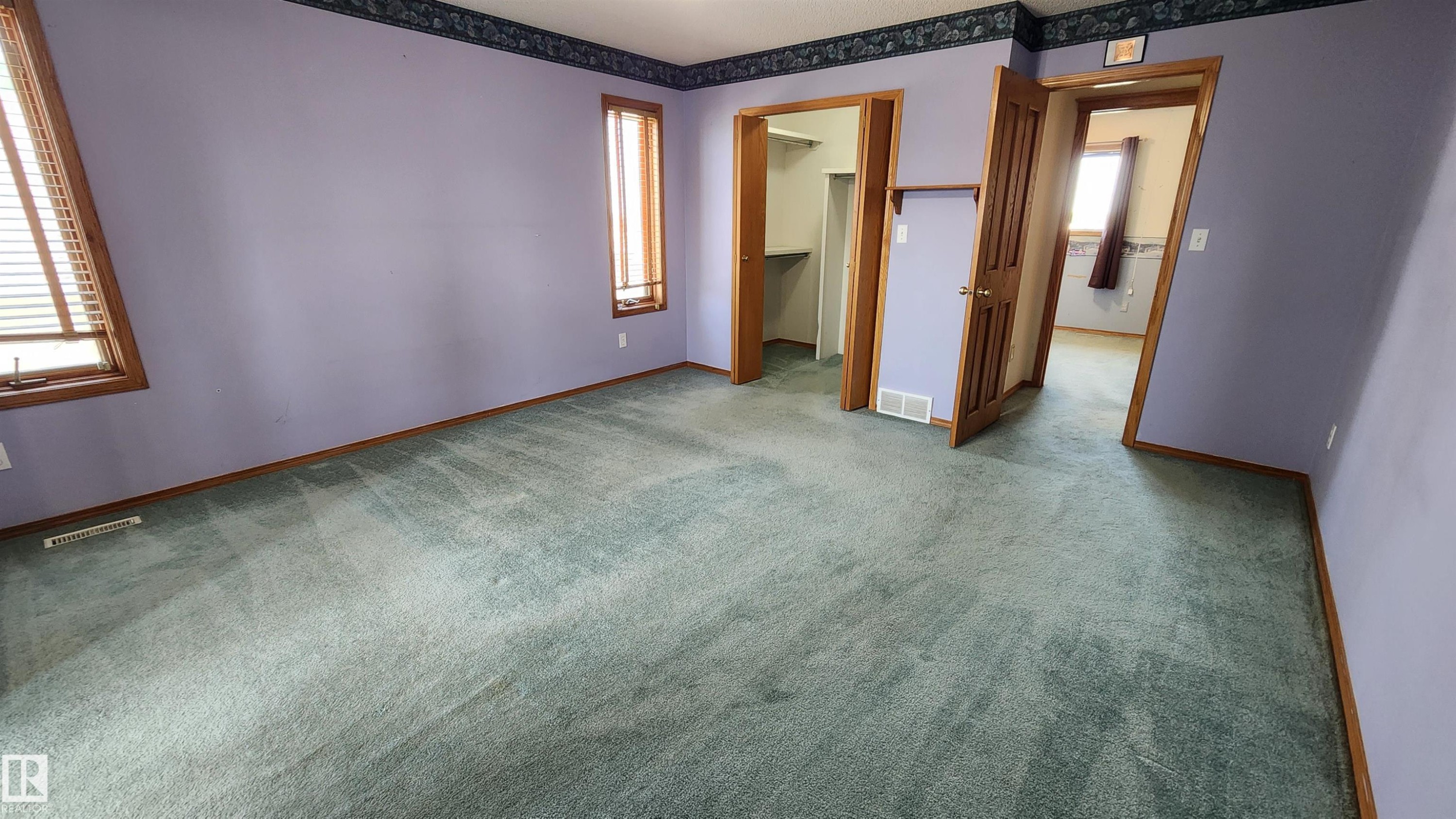 Room featuring teal-toned carpeting, two windows with wood blinds and wood trim, and a built-in closet with shelving - 2708 44A Avenue, Edmonton, AB