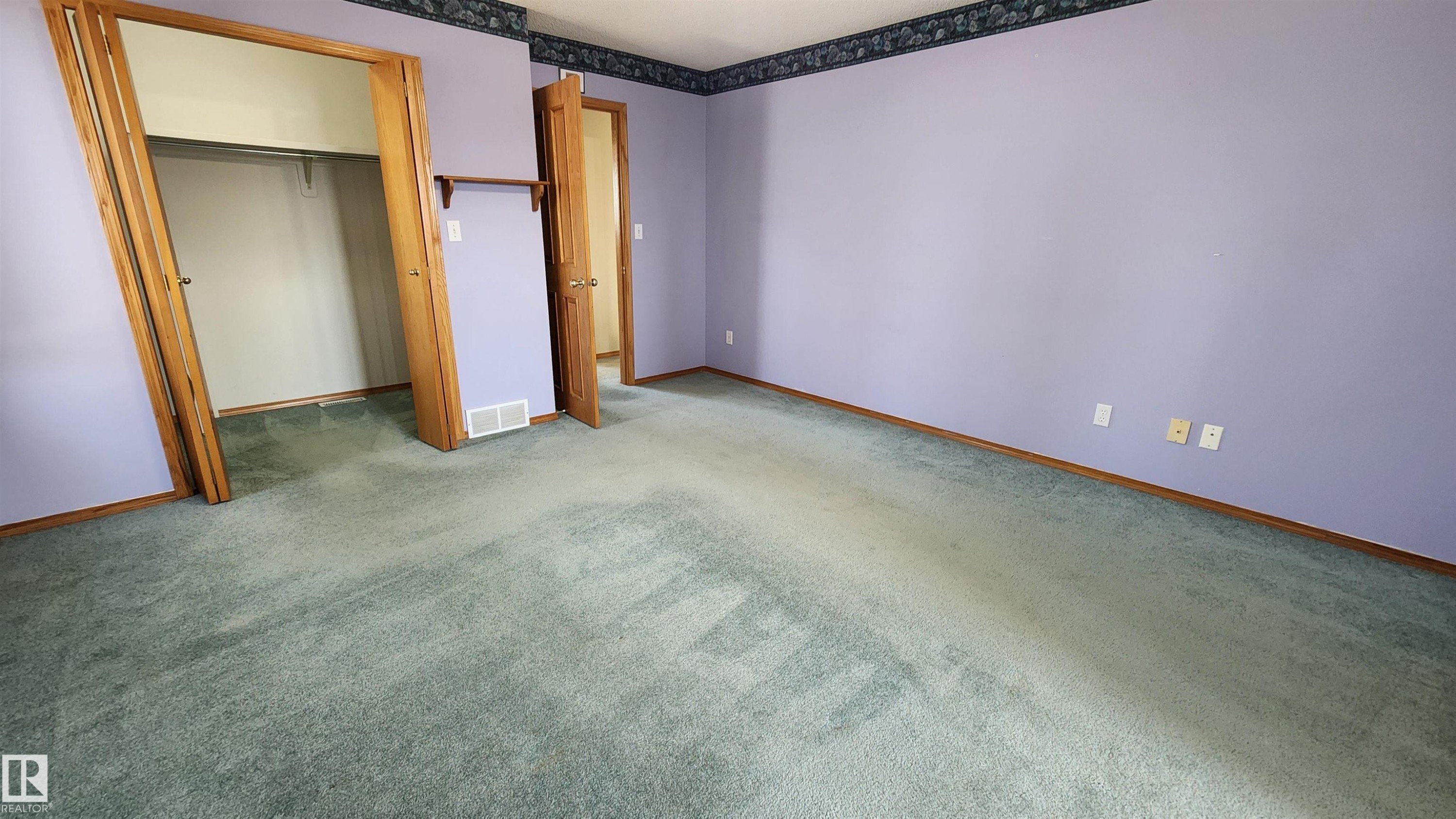 Spacious room featuring lavender walls, green carpeting, natural wood trim, and a decorative wallpaper border - 2708 44A Avenue, Edmonton, AB