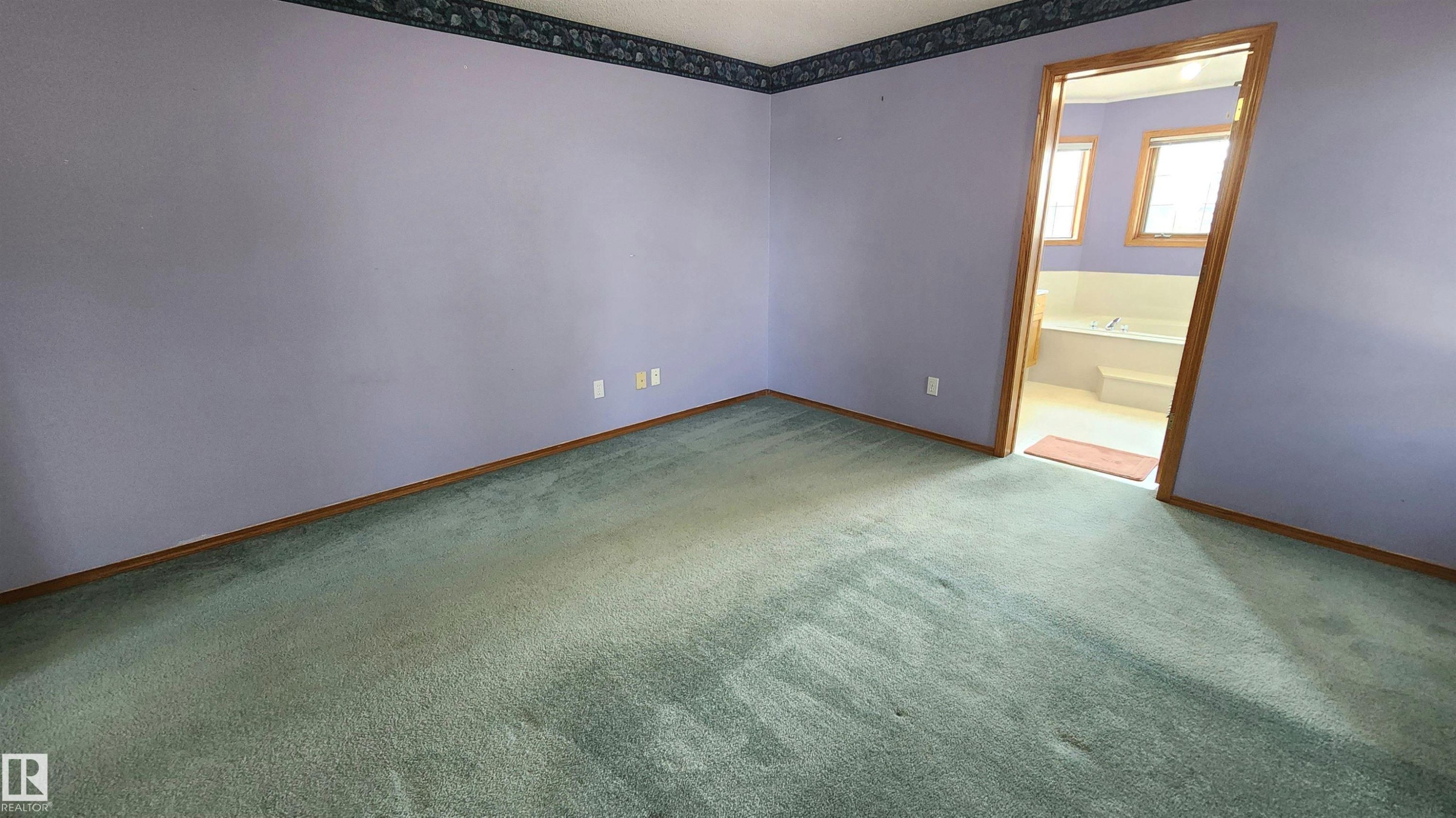 Carpeted room with a doorway opening to a bathroom featuring a built-in tub and windows - 2708 44A Avenue, Edmonton, AB