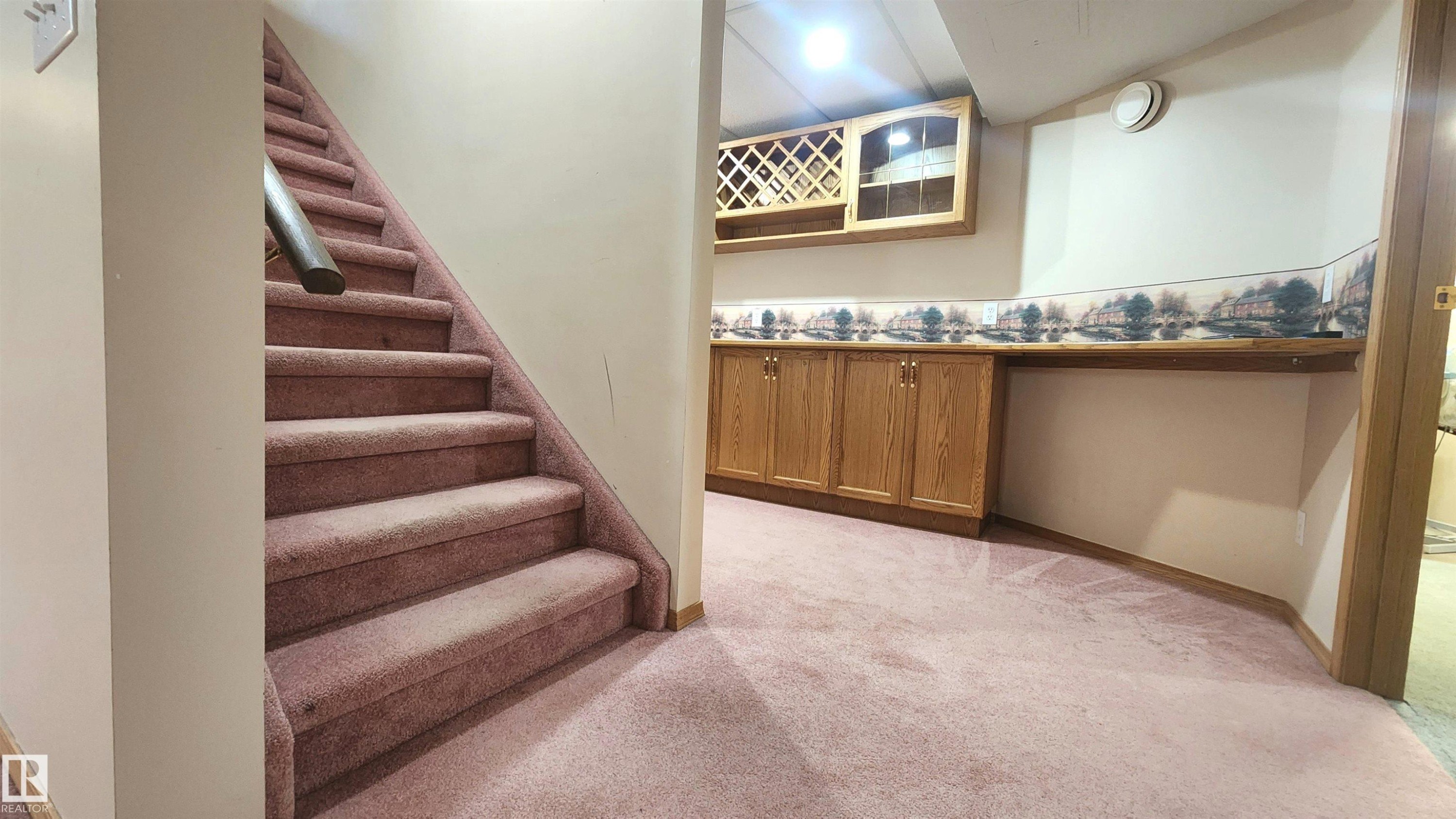 Lower-level recreation area featuring wood-finish cabinetry with built-in wine rack, a coordinating wall shelf, and pink carpet flooring - 2708 44A Avenue, Edmonton, AB