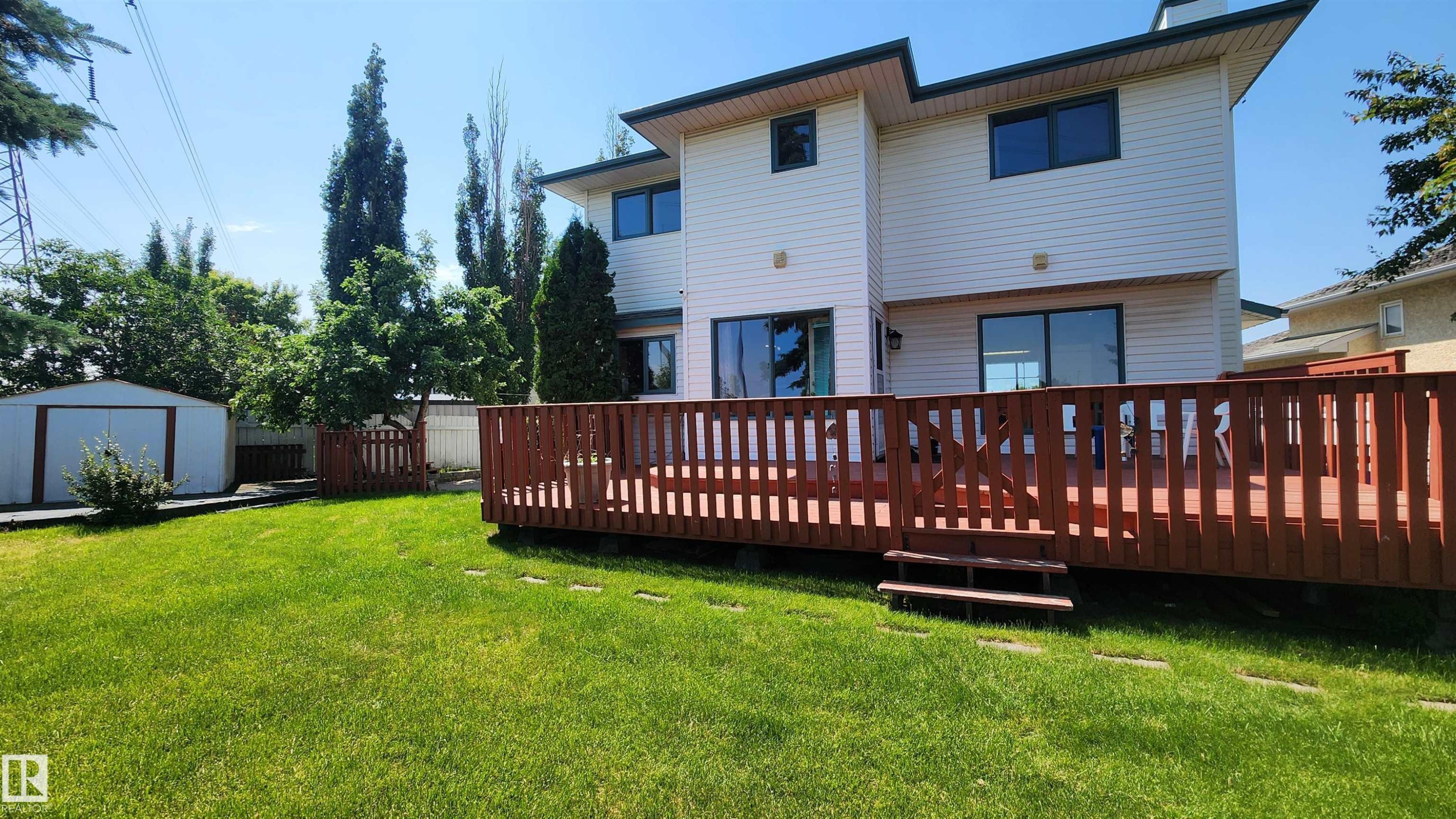 Spacious backyard featuring a substantial wood deck with railings and steps, a manicured lawn, and a white metal storage shed - 2708 44A Avenue, Edmonton, AB