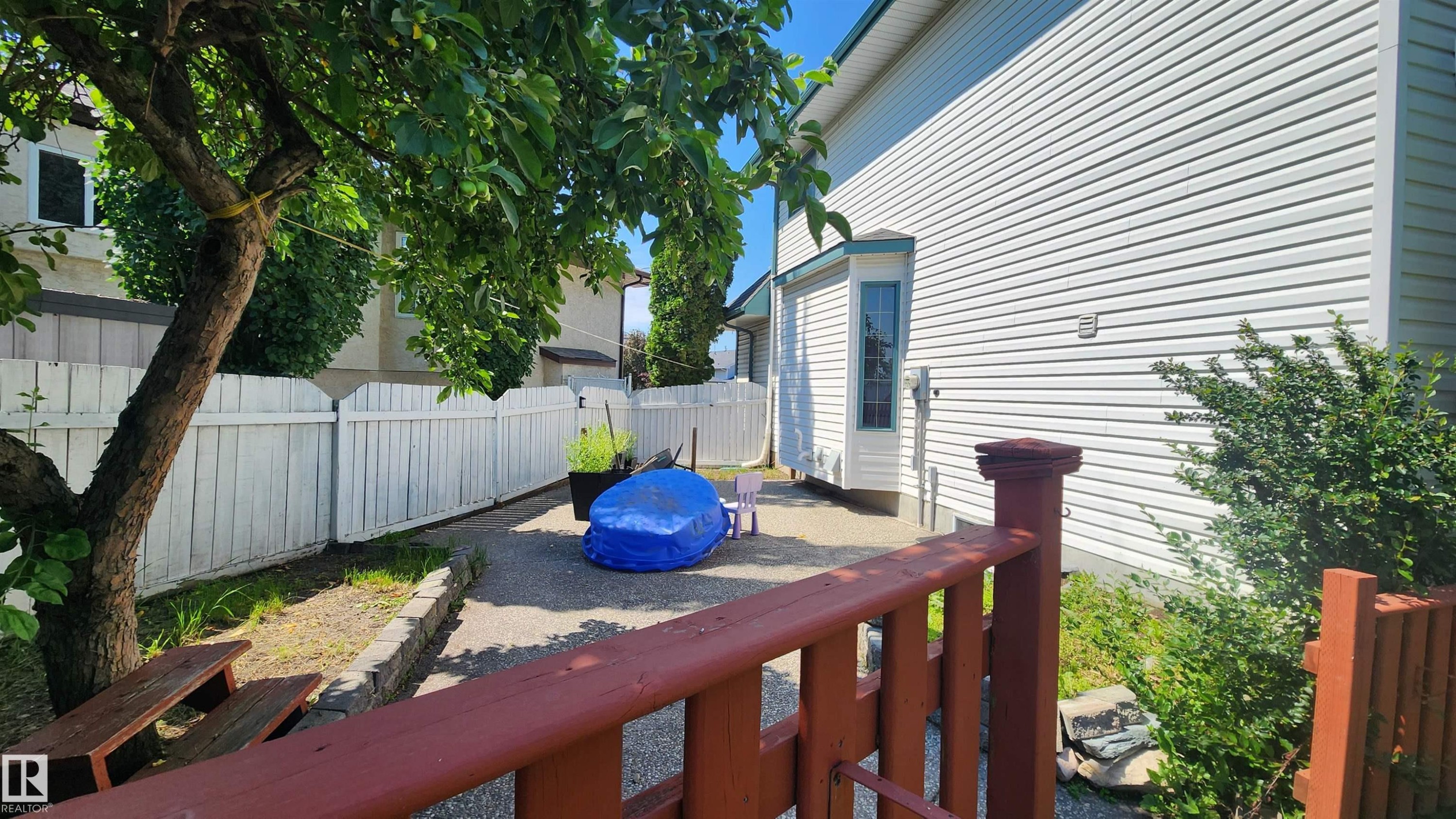 Private side yard featuring a paved patio area, white picket fence, and mature tree providing shade - 2708 44A Avenue, Edmonton, AB